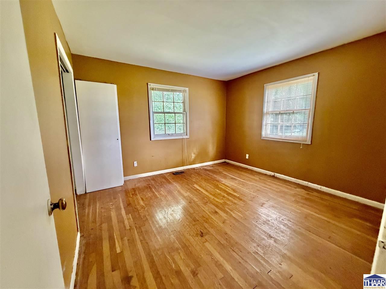 Empty room with worn hardwood floors, brown walls, and two windows.