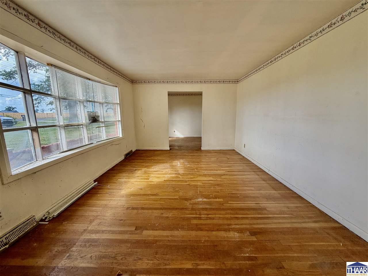 Empty living room with hardwood floors, large windows, and a doorway to another room.