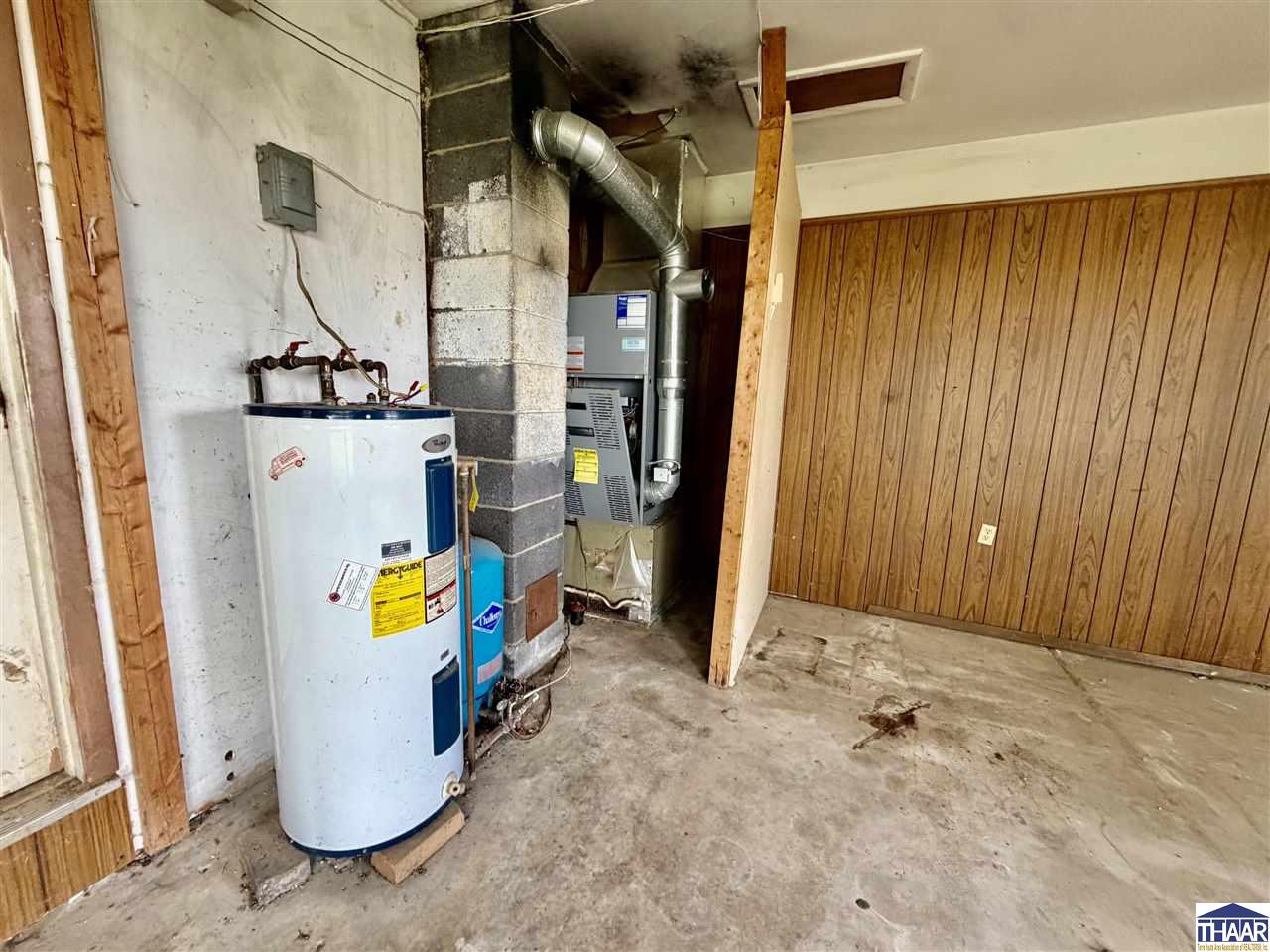 Utility room with a water heater, furnace, exposed ductwork, and wood-paneled walls.