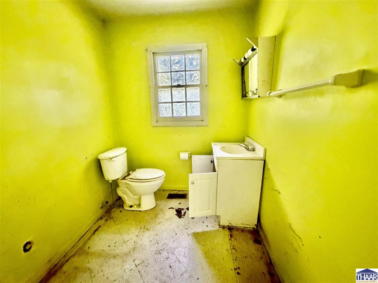 Vacant yellow bathroom with a toilet, small sink vanity, and window.
