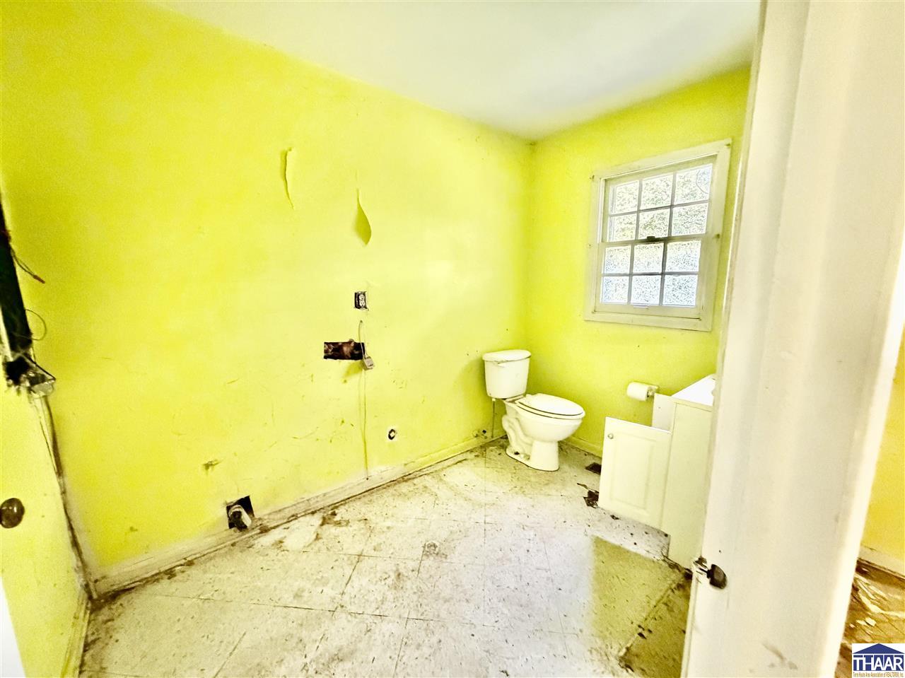 Unfinished bathroom with bright yellow walls, exposed openings, a toilet, and a small window.