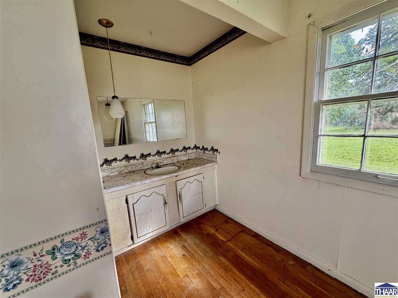 Empty bathroom with a white vanity, ornate mirror, floral tile border, and tall window.