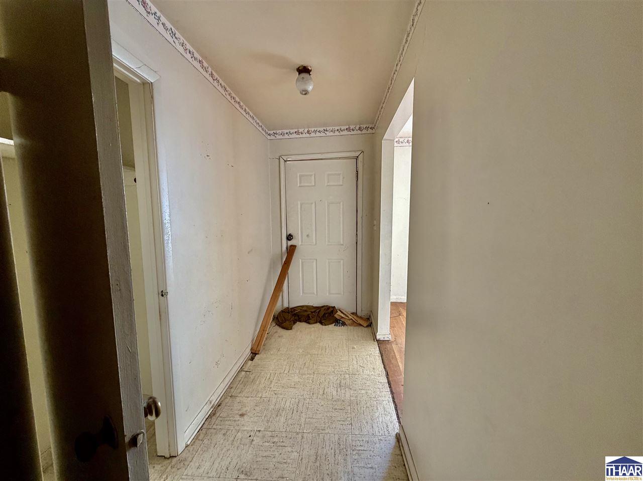 Worn hallway with a closed white door, scuffed walls, and debris on the floor.