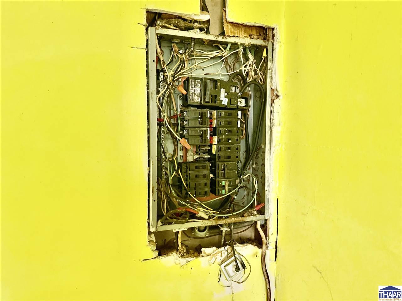 Electrical breaker panel with exposed wiring and damaged yellow wall