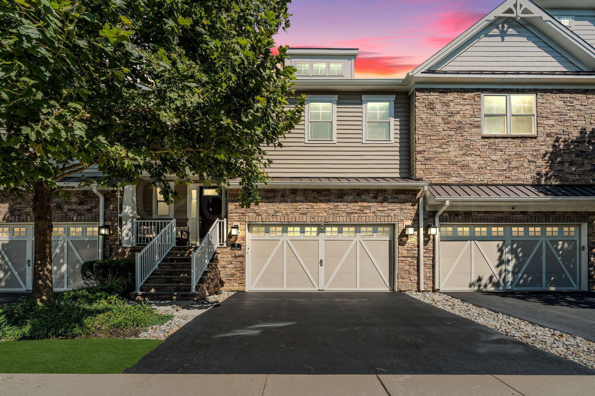 Two-story stone-and-siding house with three garage doors beneath a pink dusk sky.