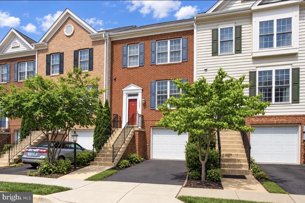 Brick townhouse with a red front door, front steps, and attached garage among neighboring homes.