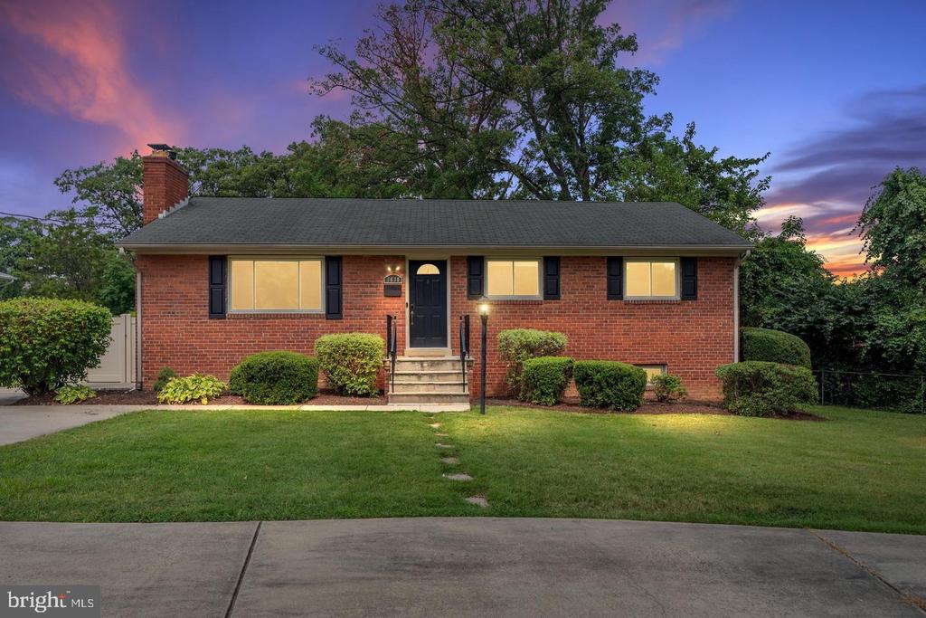 Single-story red brick house with a centered entry, trimmed shrubs, and lawn at dusk.