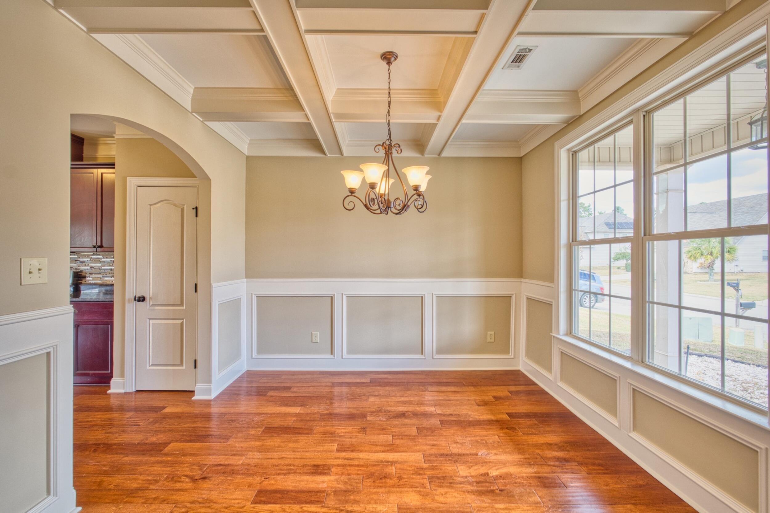 Empty dining room with a coffered ceiling, chandelier, wood floors, and large windows.