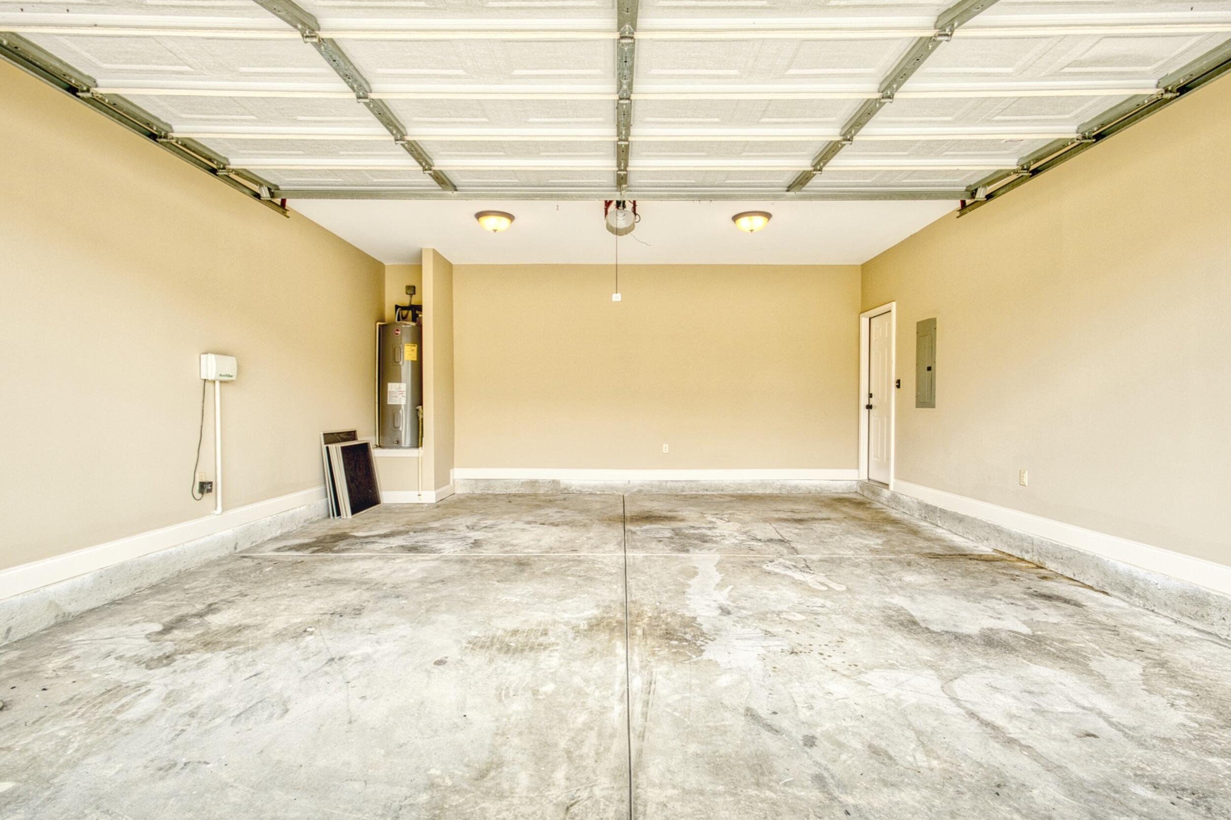 Empty garage with an open overhead door, concrete floor, and water heater.