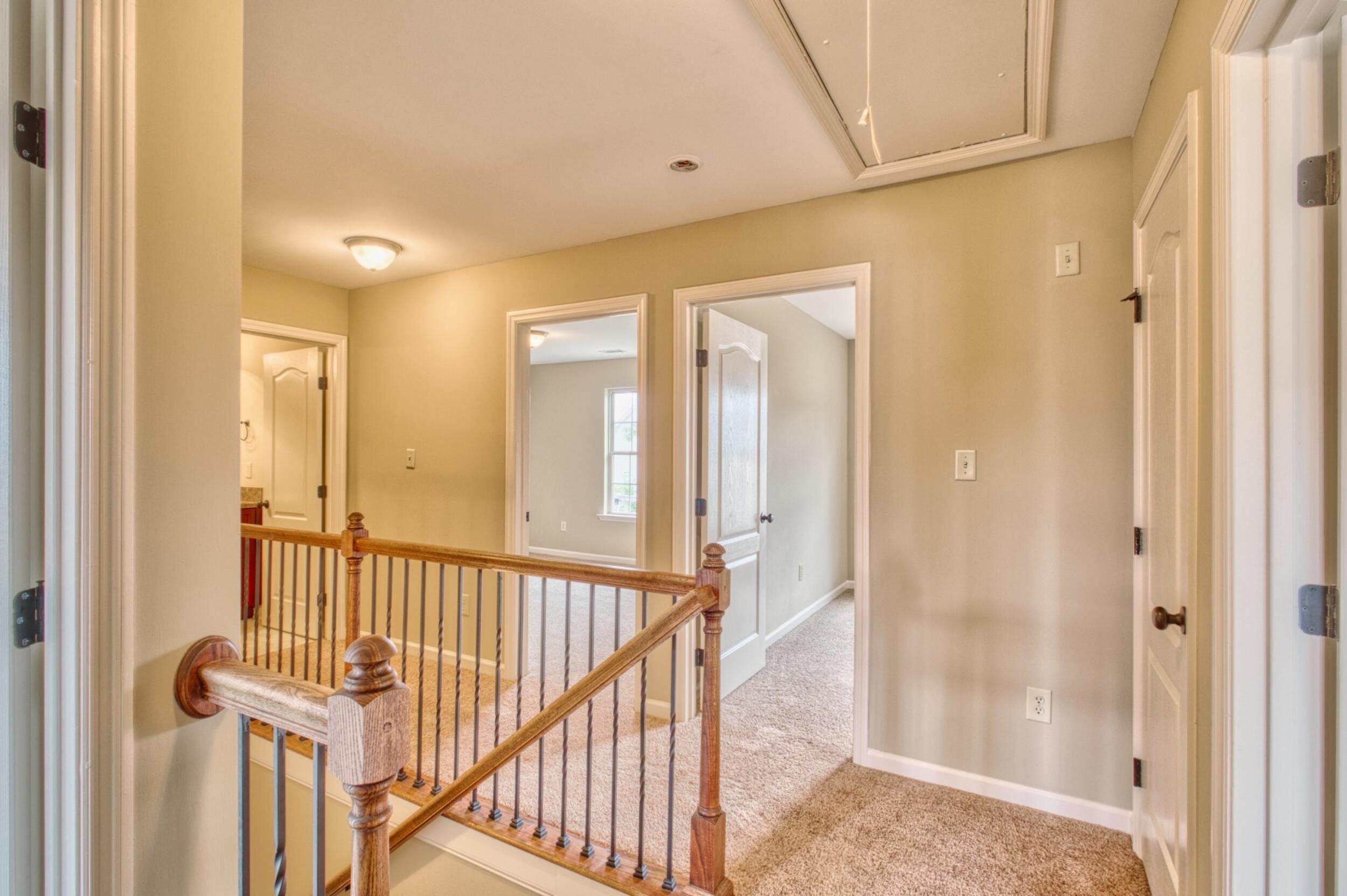 Upstairs landing with carpeted floors, a wooden stair railing, and open doorways.