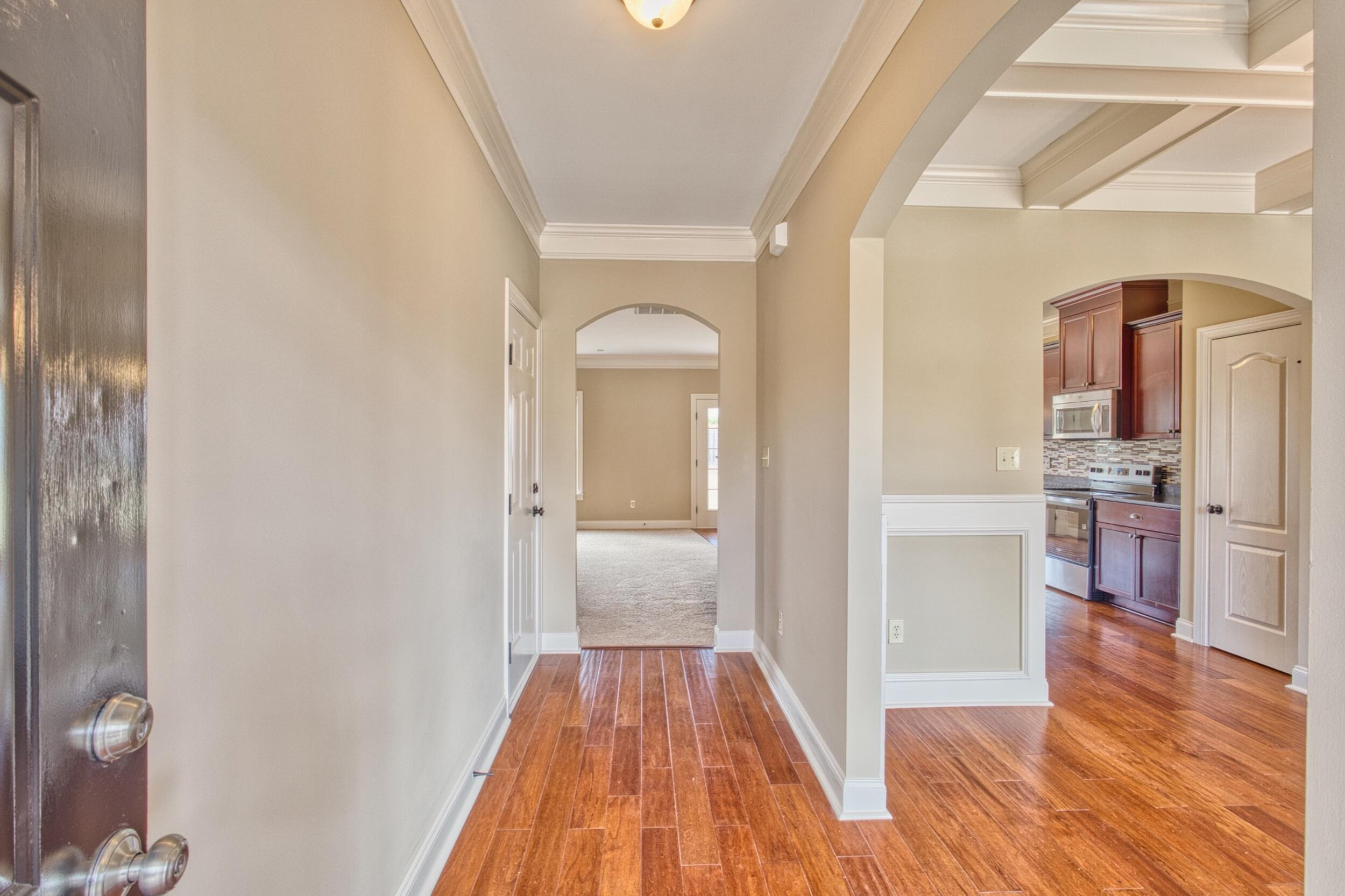 Entry hallway with wood-look floors and arched openings leading to a kitchen with dark cabinets.