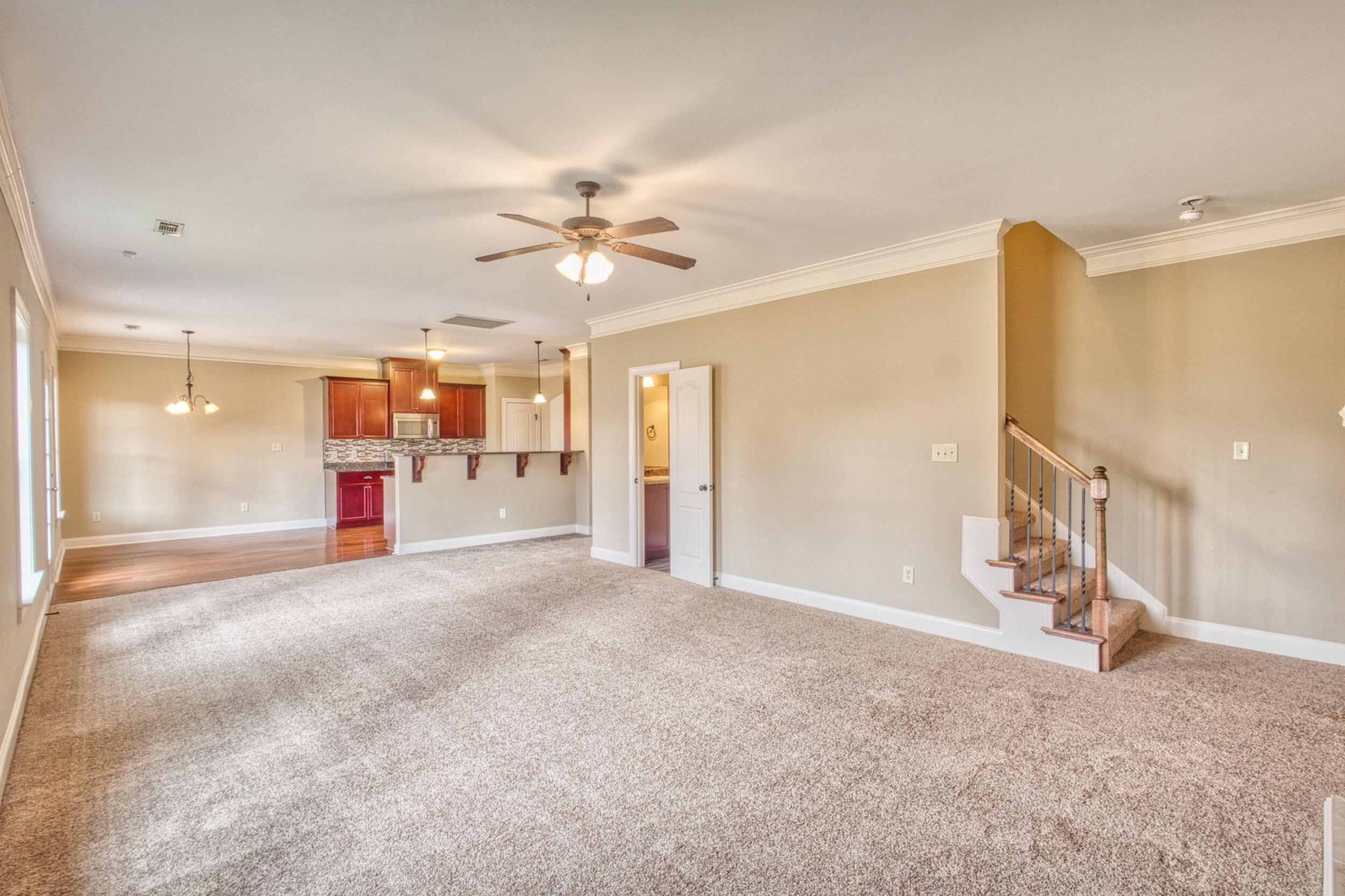 Unfurnished living room with carpet, open kitchen, and staircase with wood-and-metal railing.