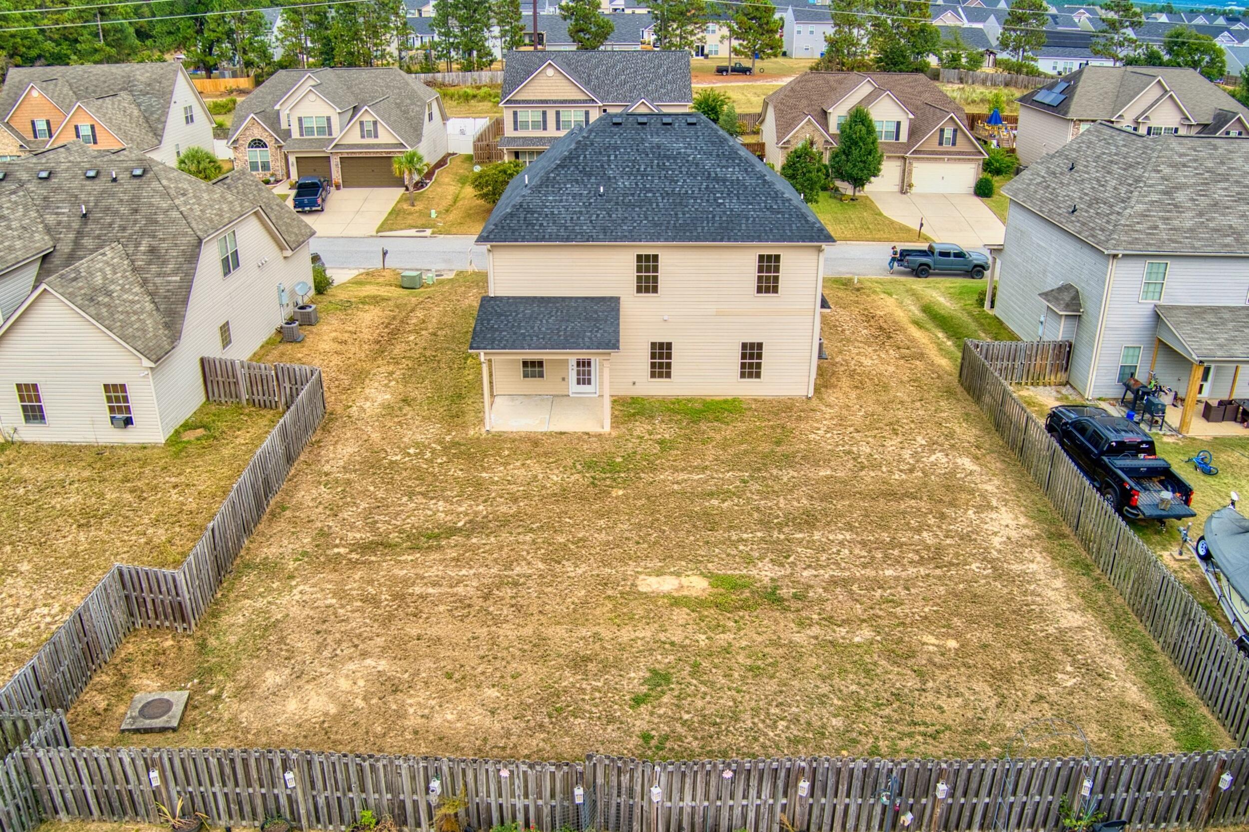 Aerial view of a beige two-story house and its large fenced backyard, with neighboring homes beyond.