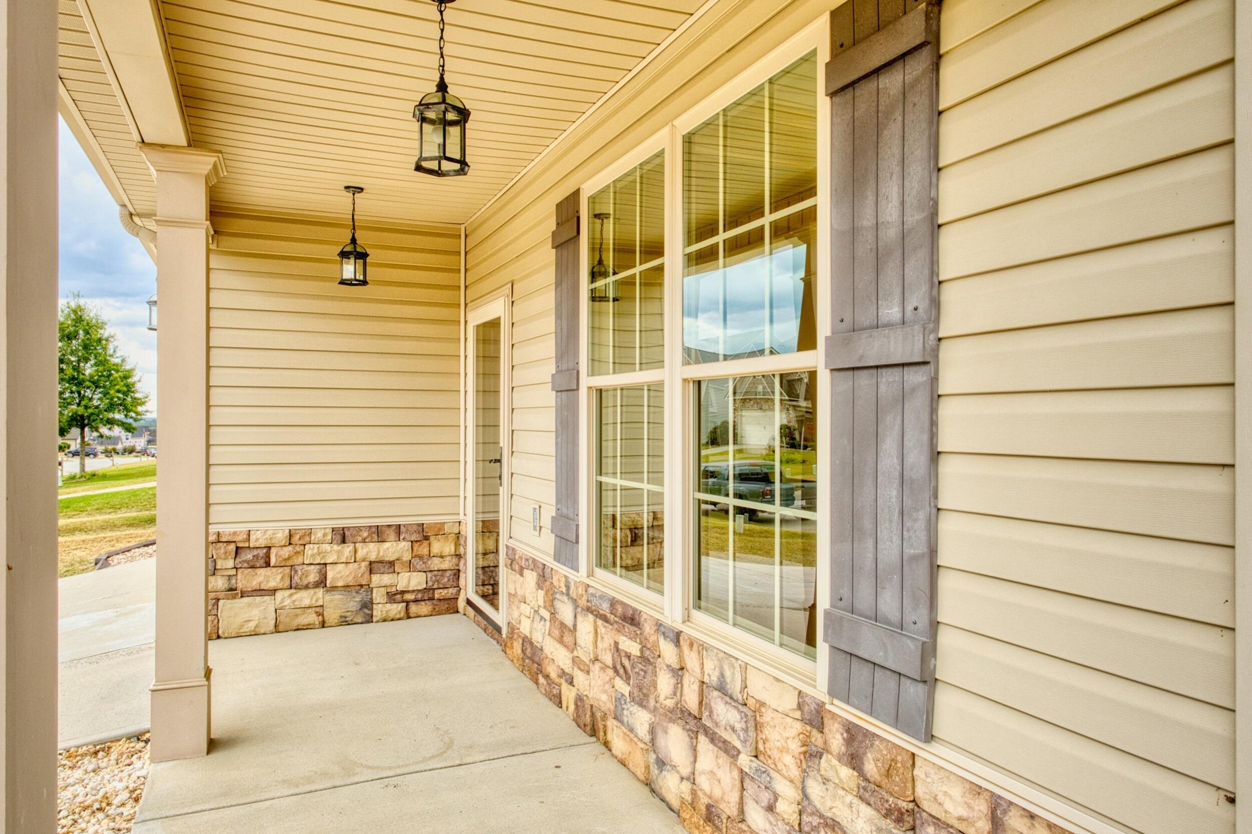 Covered porch with stone veneer, large windows, gray shutters, and hanging lanterns.