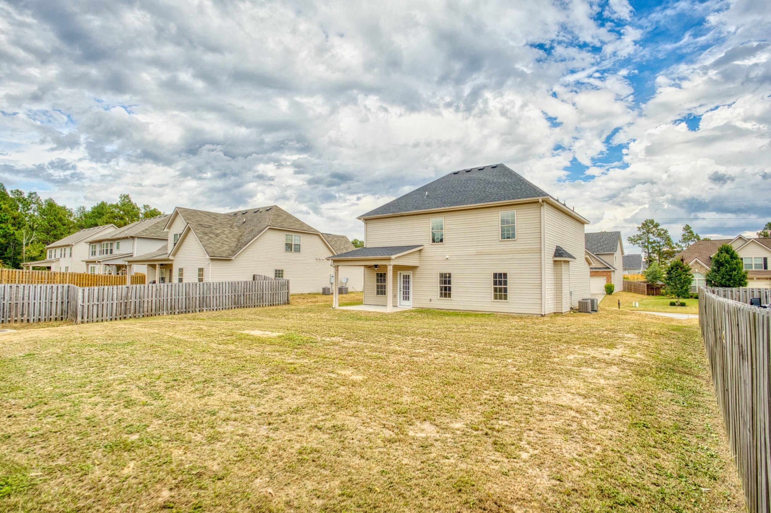 Rear of a two-story beige house with a covered patio and broad fenced backyard.