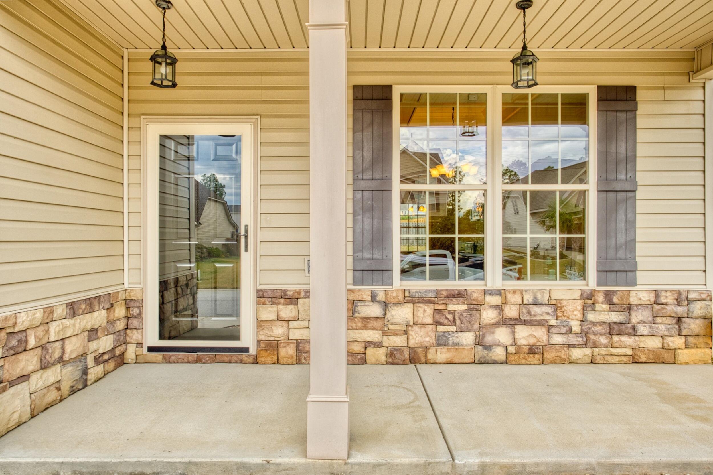 Covered front porch with stone veneer, beige siding, large windows, and hanging lanterns.