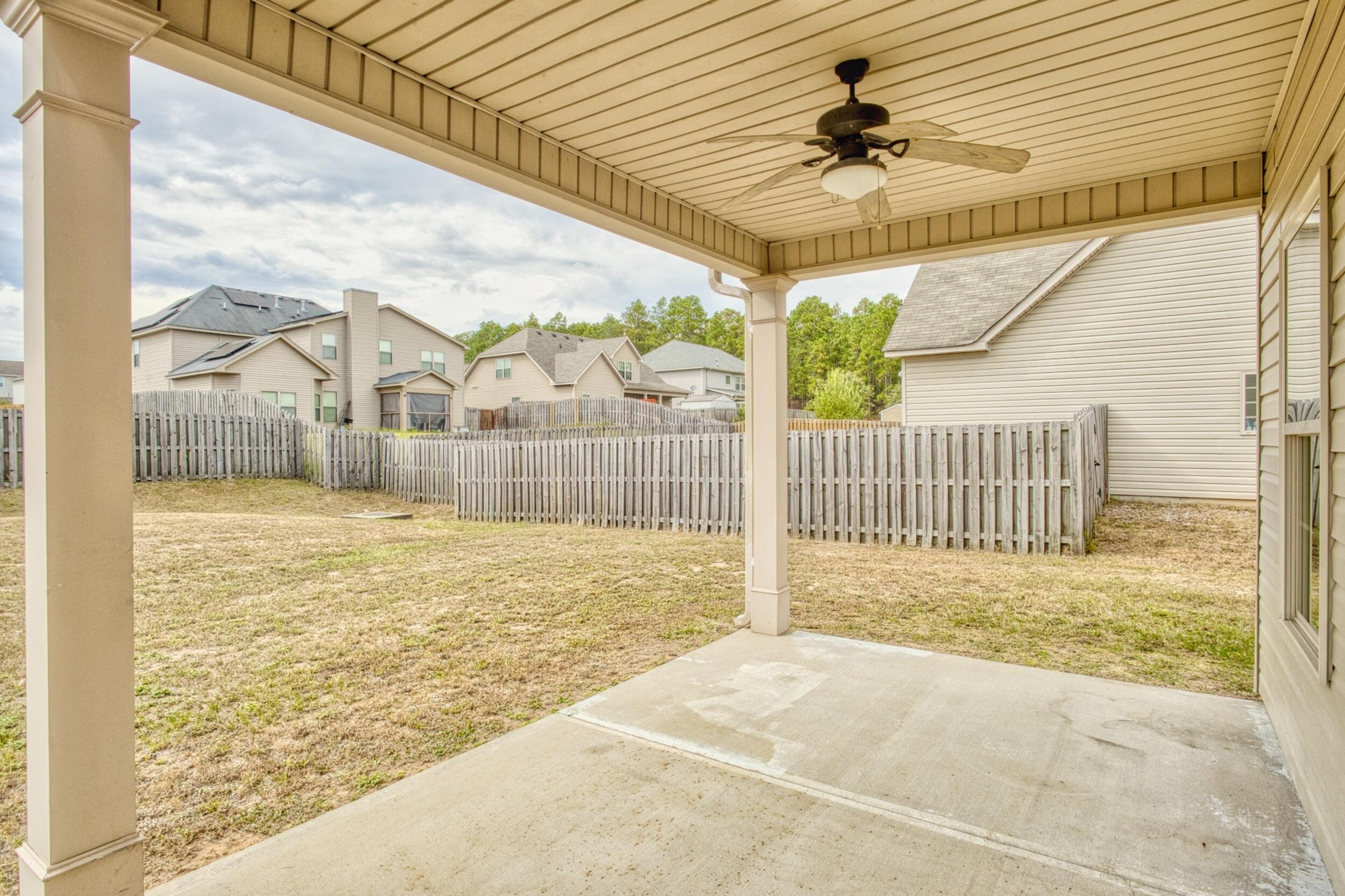 Covered concrete patio with ceiling fan overlooking a fenced backyard and neighboring homes.
