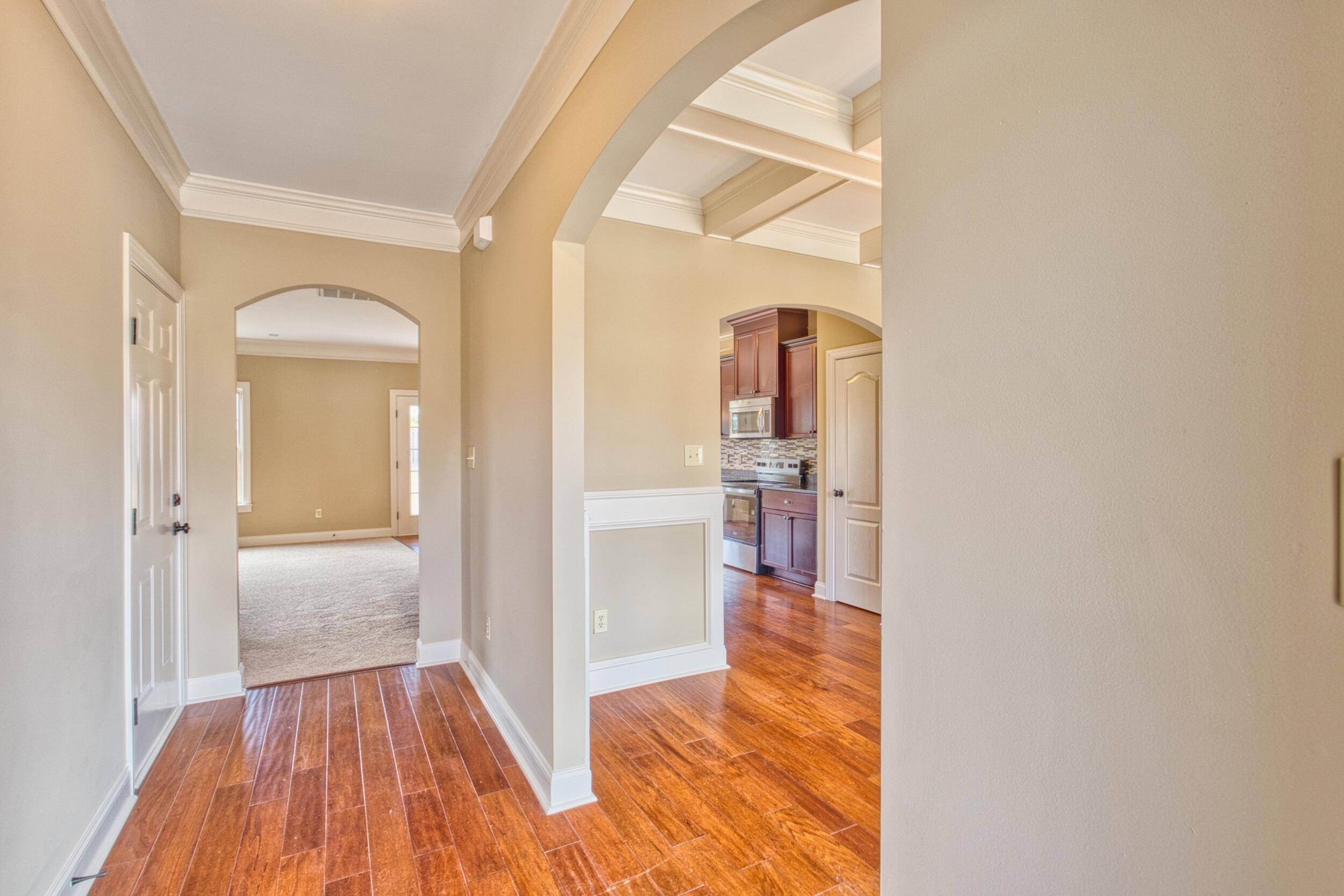 Entry hall with arched openings, warm plank flooring, and a view into the kitchen.