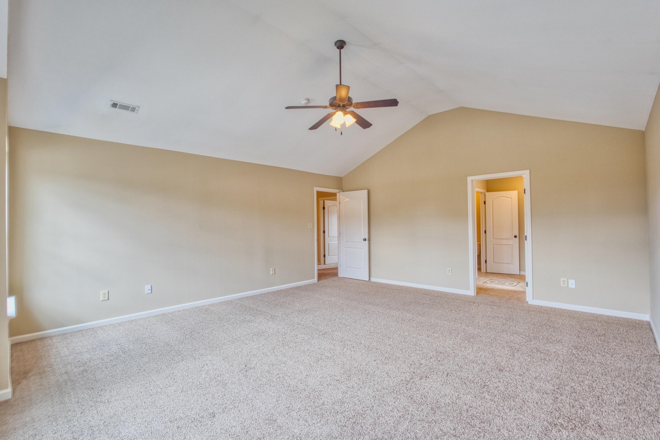 Empty carpeted bedroom with a vaulted ceiling, ceiling fan, and two open doorways.