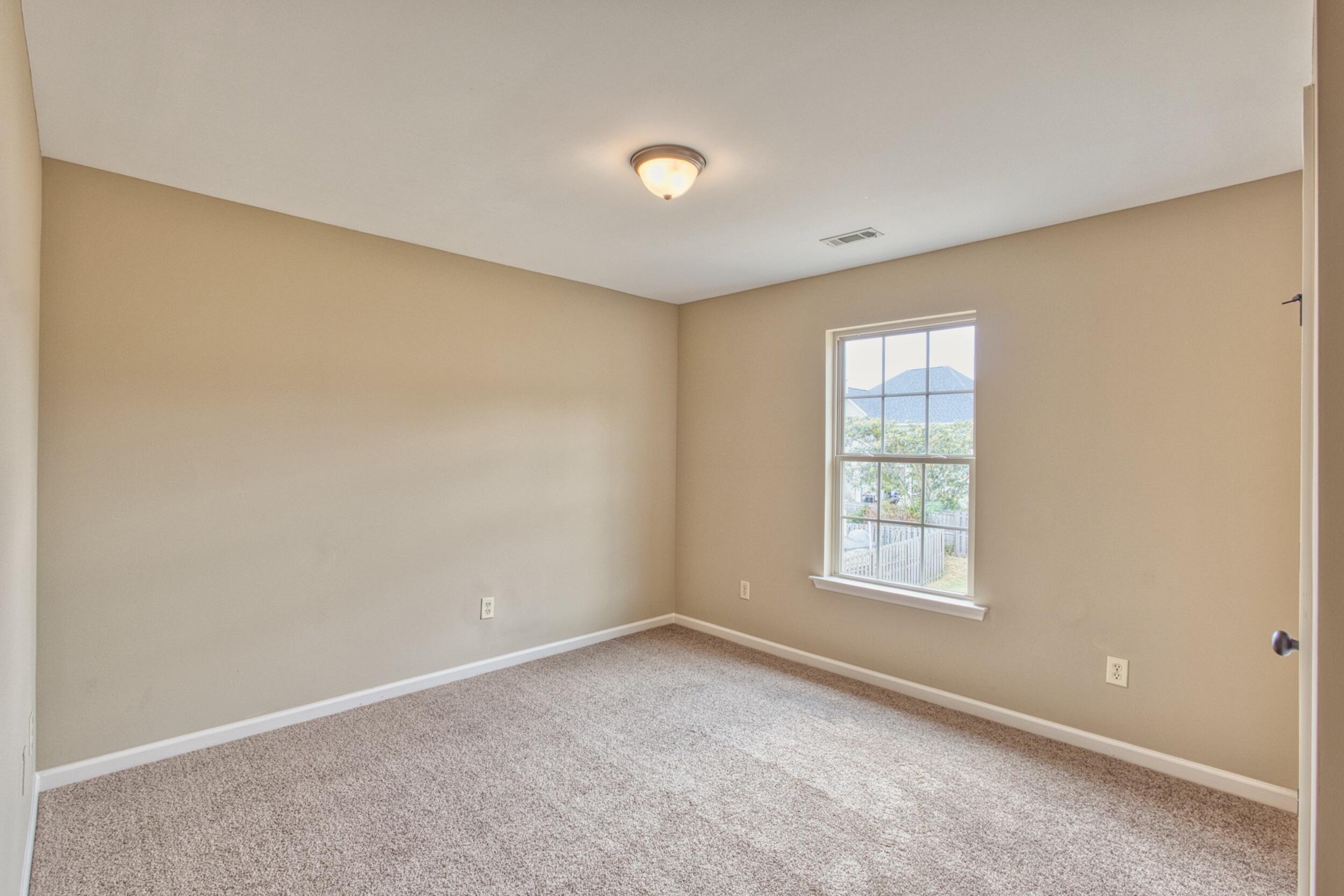 Empty carpeted room with beige walls and a window letting in daylight.