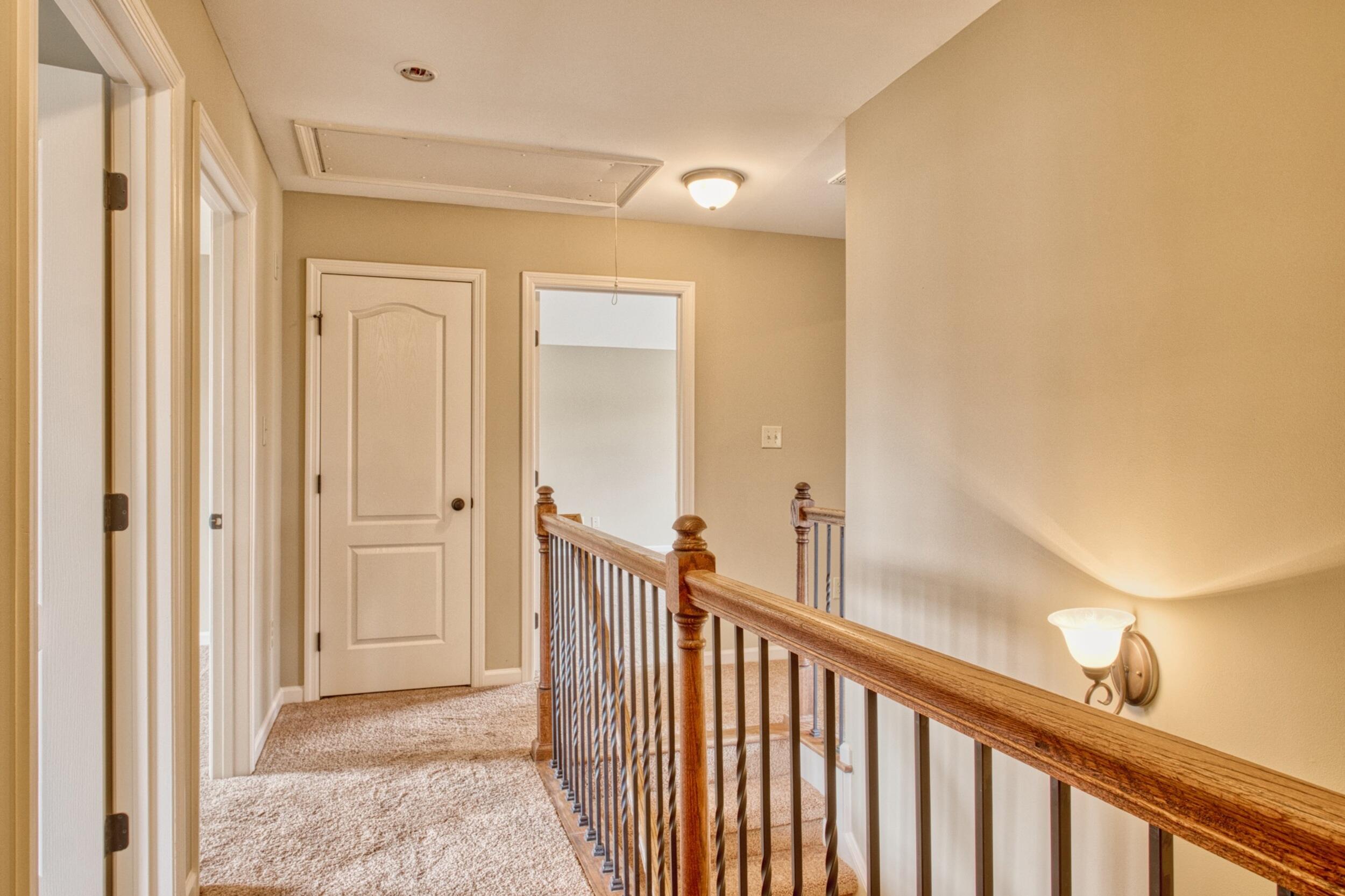 Upstairs landing with beige carpet and a wooden railing along the open staircase.