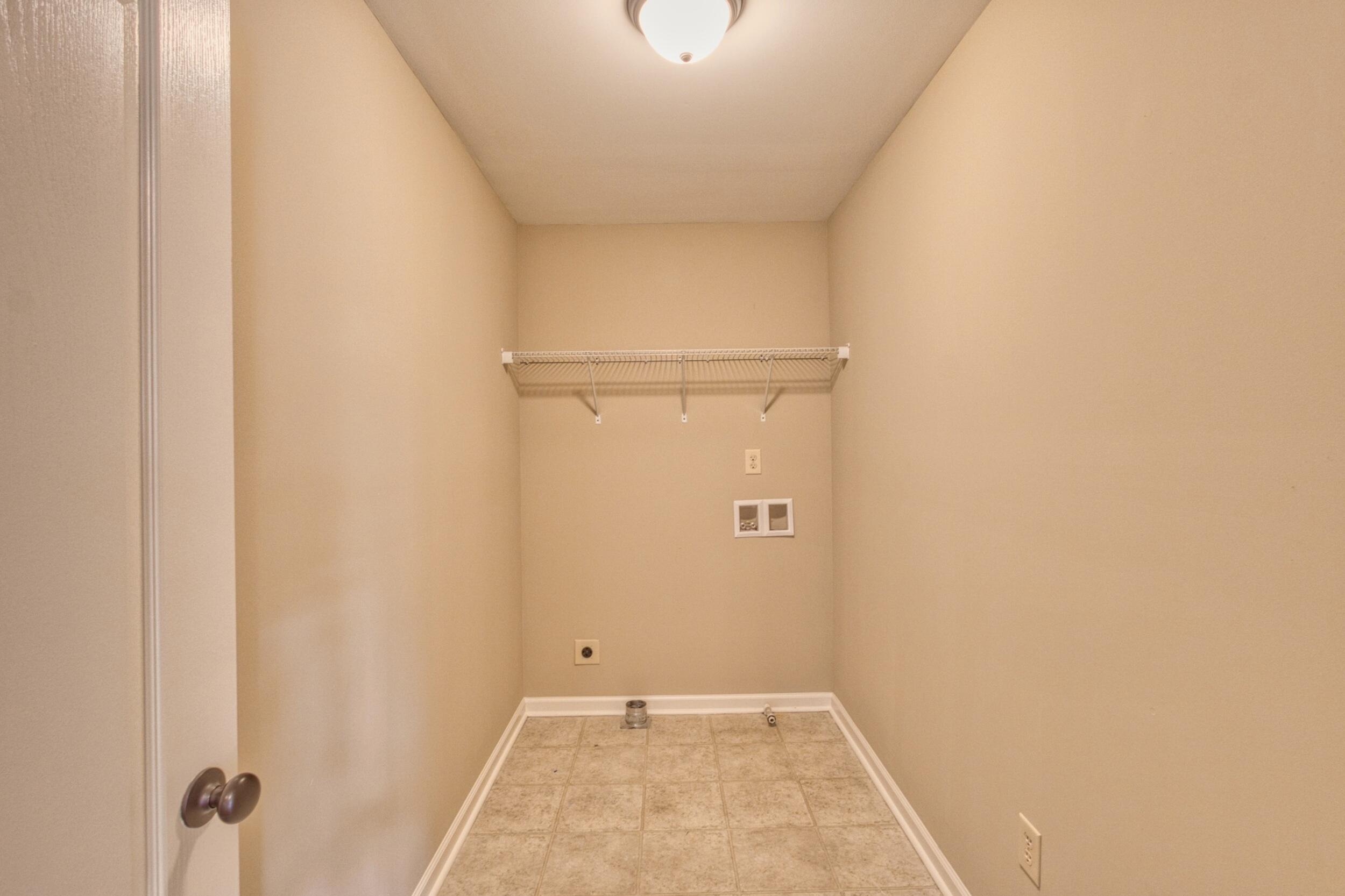 Empty laundry room with a wire shelf, washer and dryer hookups, and tiled floor.