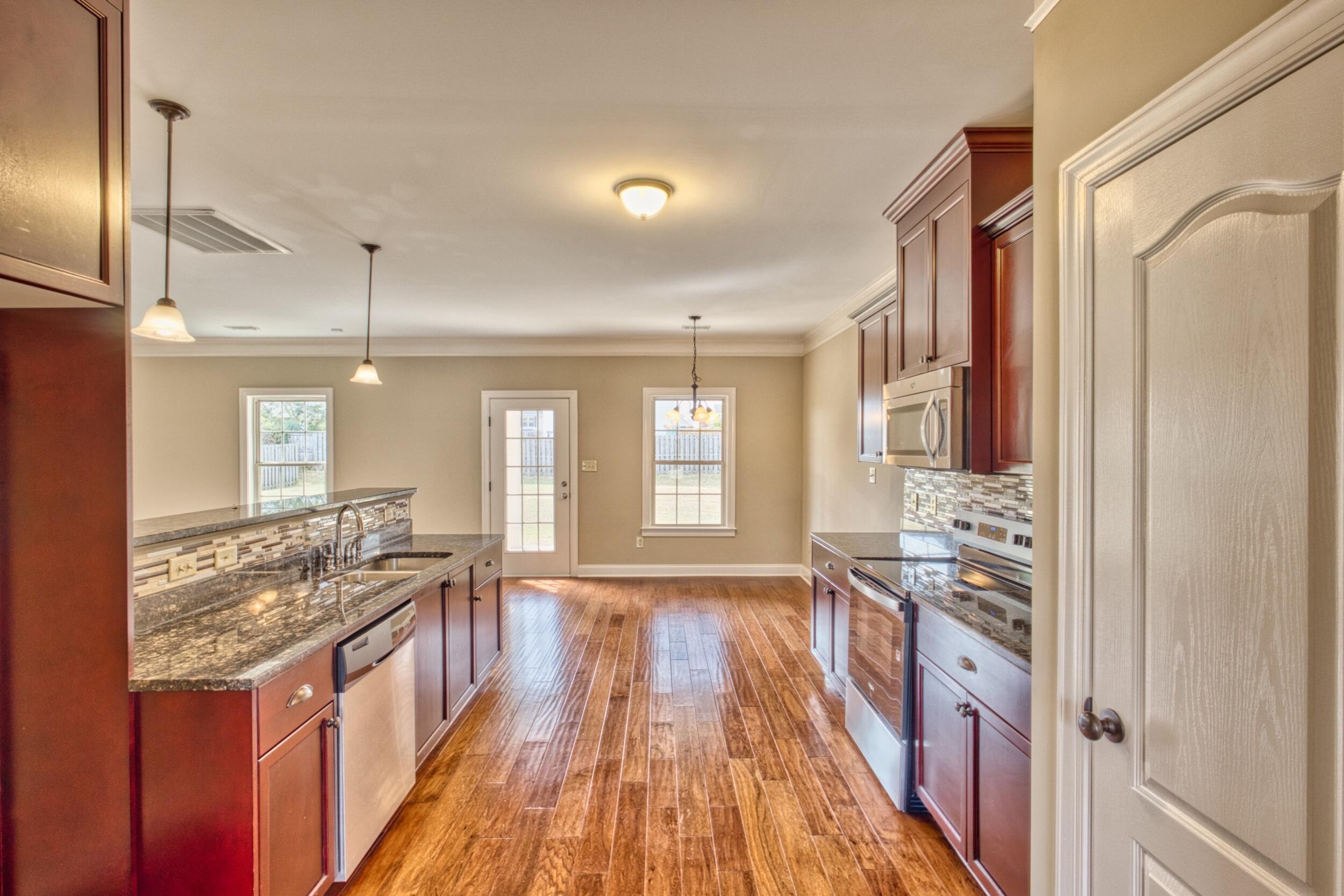 Kitchen with cherry cabinets, granite counters, stainless appliances, and a long wood-look tile floor.