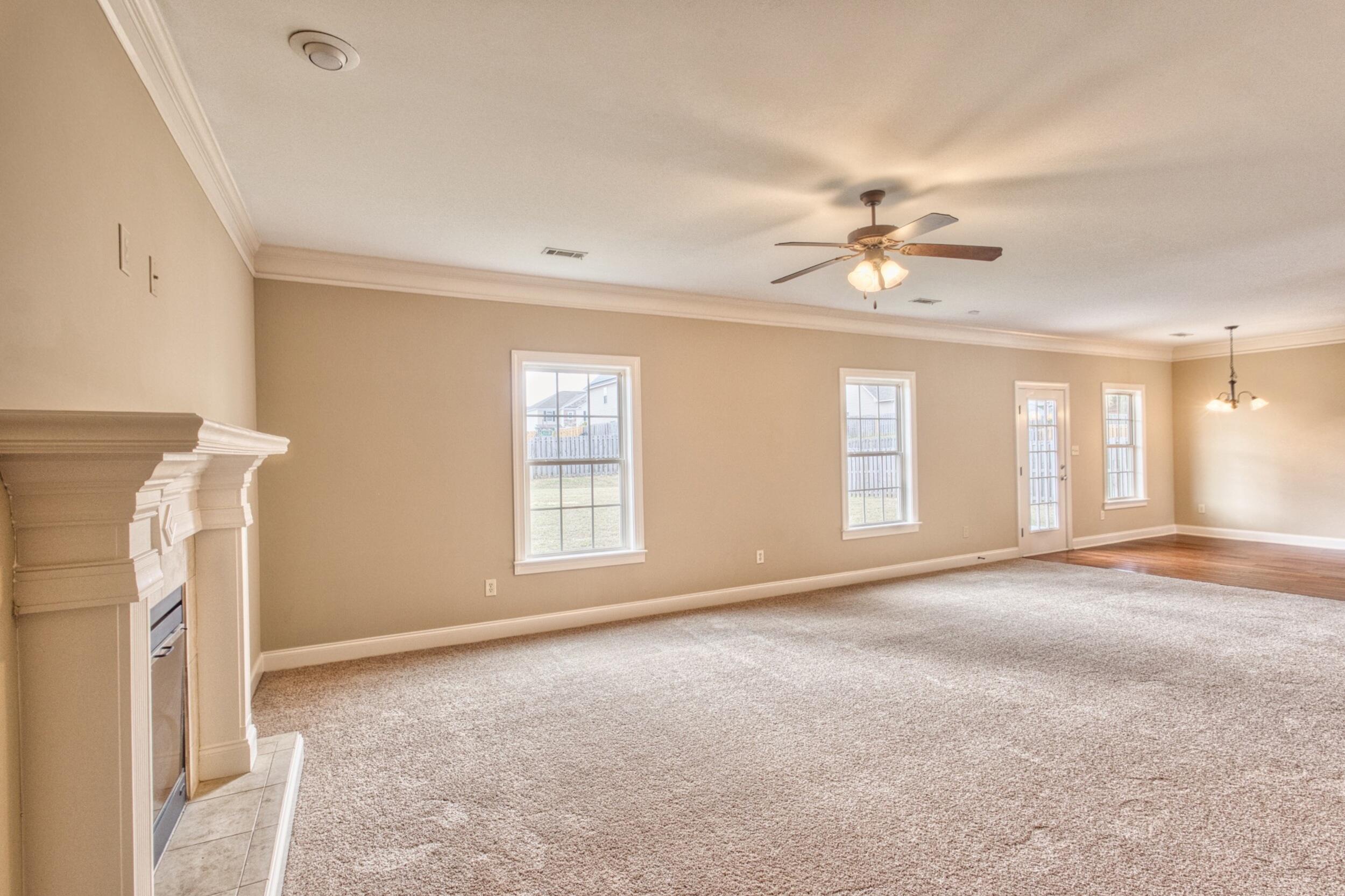 Empty living room with a fireplace, carpet, and windows opening to the backyard.