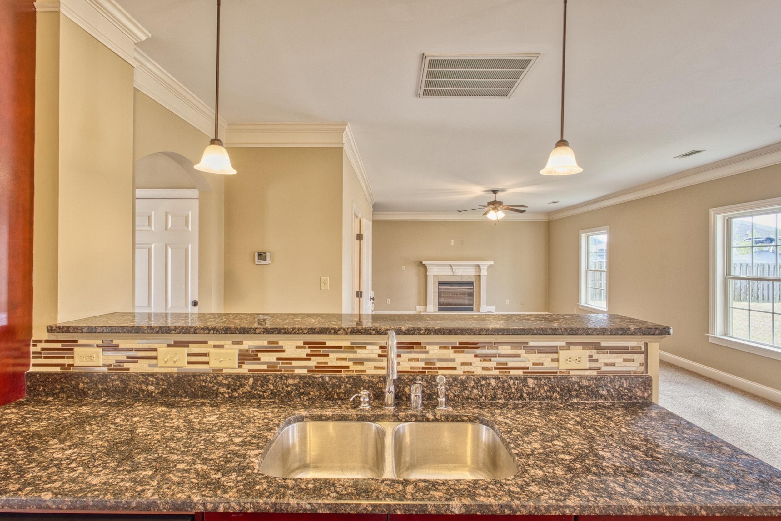 Kitchen granite peninsula and double sink overlooking an open living room with a fireplace.