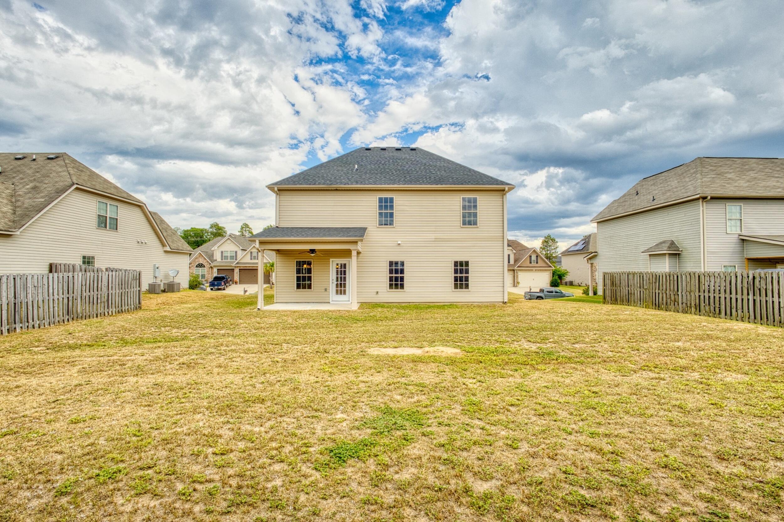 Two-story beige house behind a dry grassy backyard, with a covered patio and wooden privacy fences.
