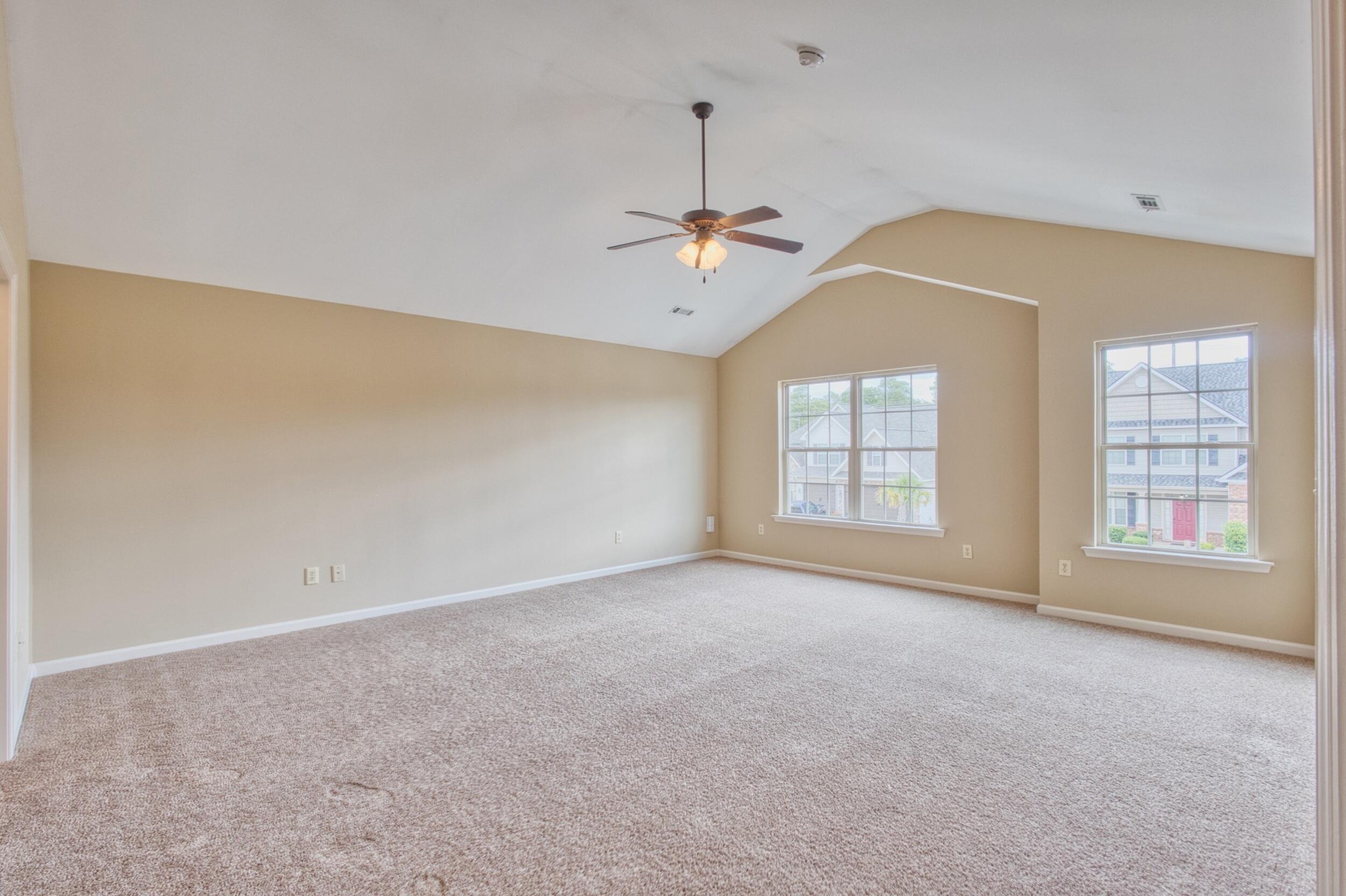 Empty carpeted room with a vaulted ceiling, ceiling fan, and two windows.