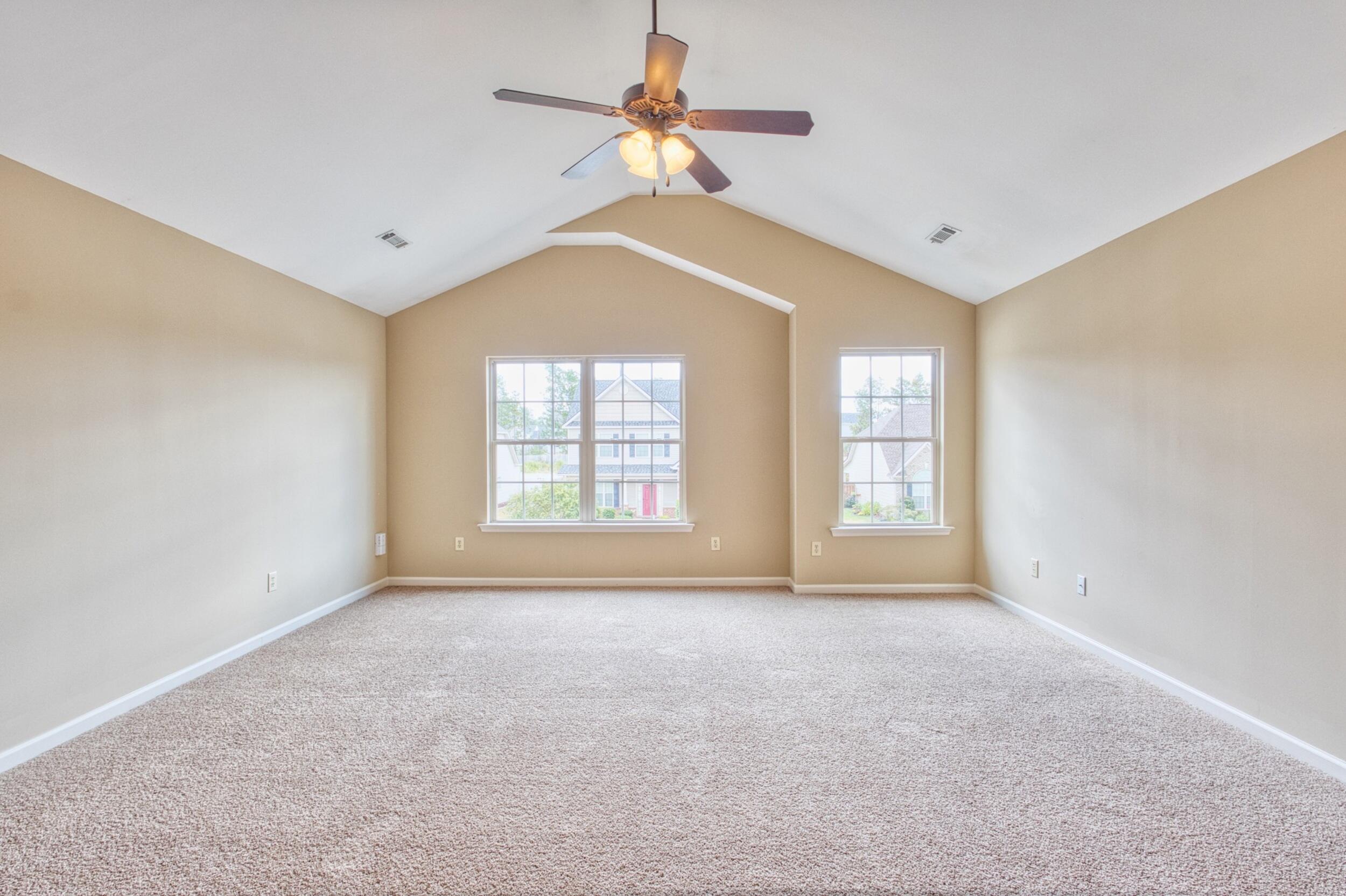 Empty bedroom with a vaulted ceiling, ceiling fan, carpet, and two windows.