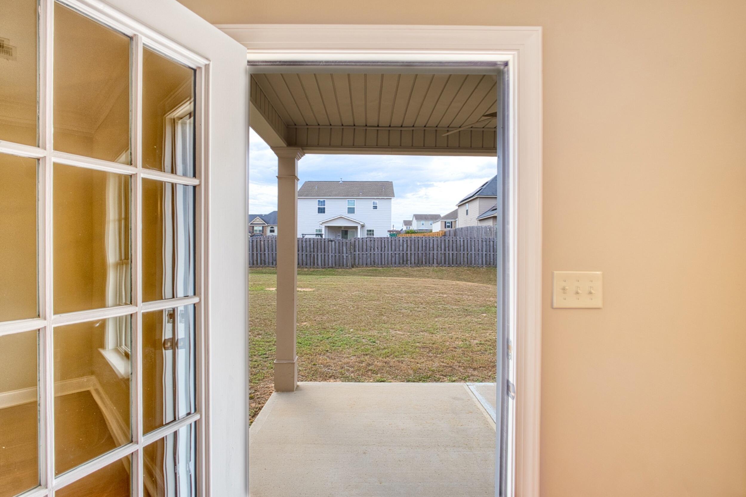 Covered patio and fenced backyard viewed through an open glass-paneled door.