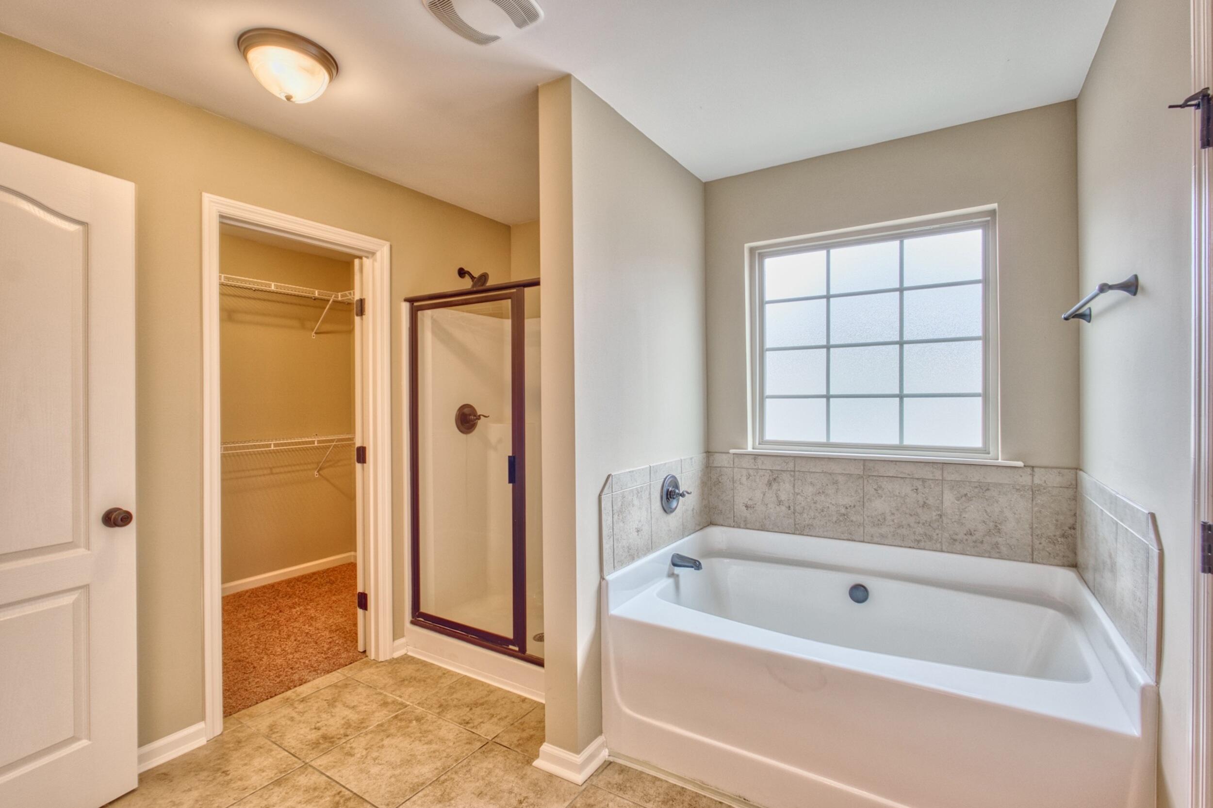 Bathroom with a large tub beneath a gridded window and an open doorway to a walk-in closet.