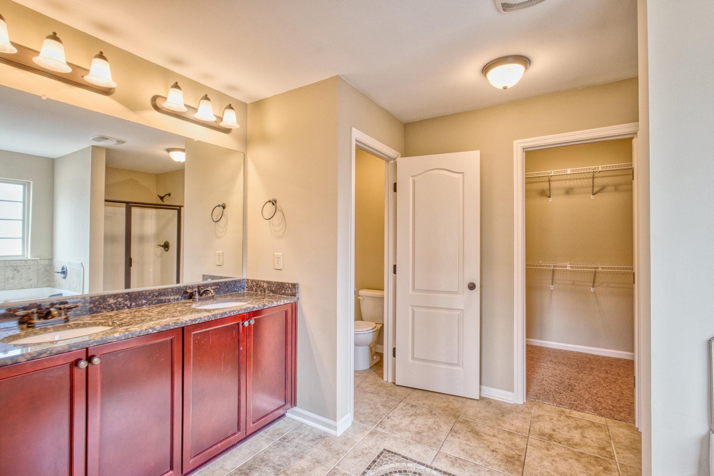 Bathroom with a double-sink burgundy vanity, granite countertop, and adjoining walk-in closet.