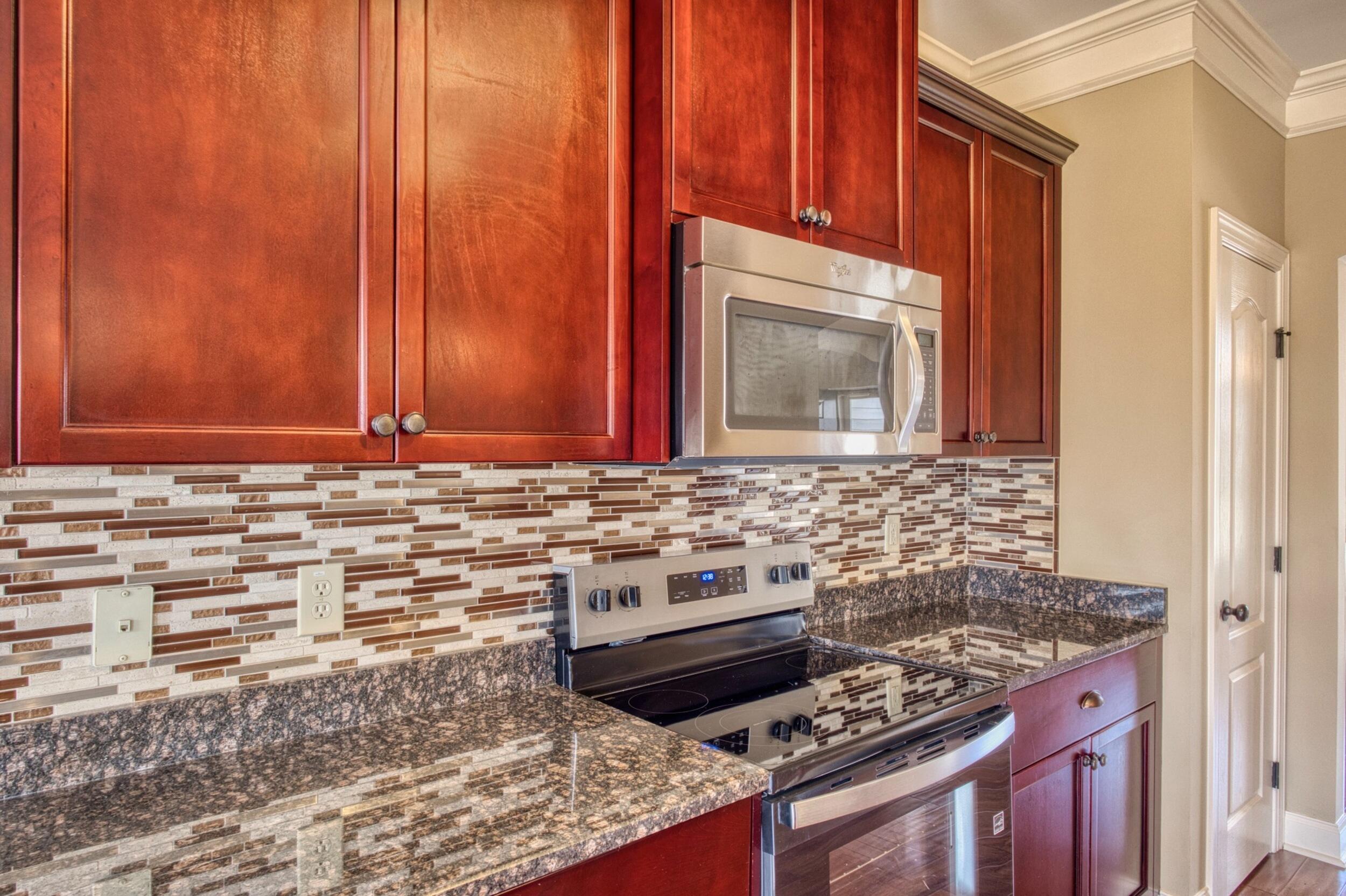 Kitchen with red wood cabinets, stainless appliances, granite counters, and a mosaic tile backsplash.