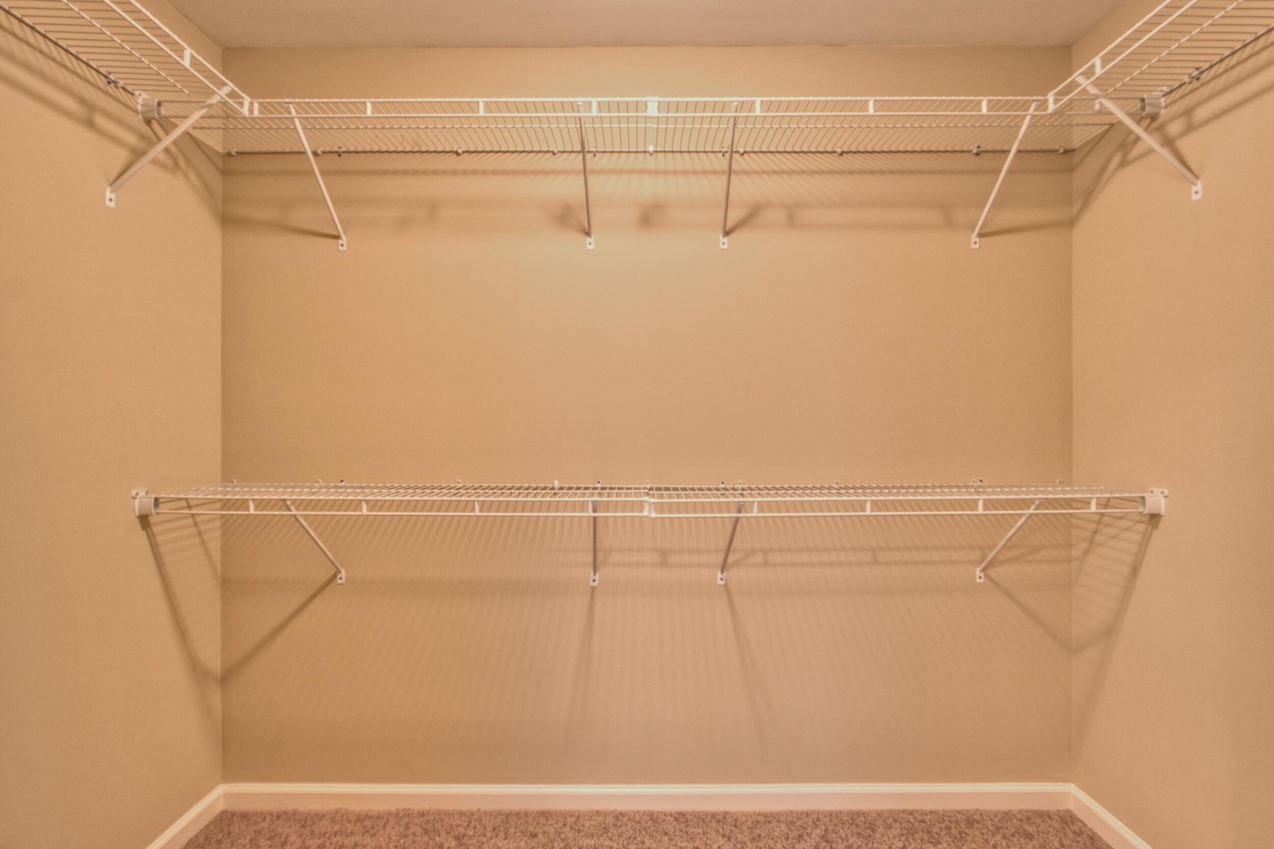 Empty walk-in closet with white wire shelving on two levels and tan walls.