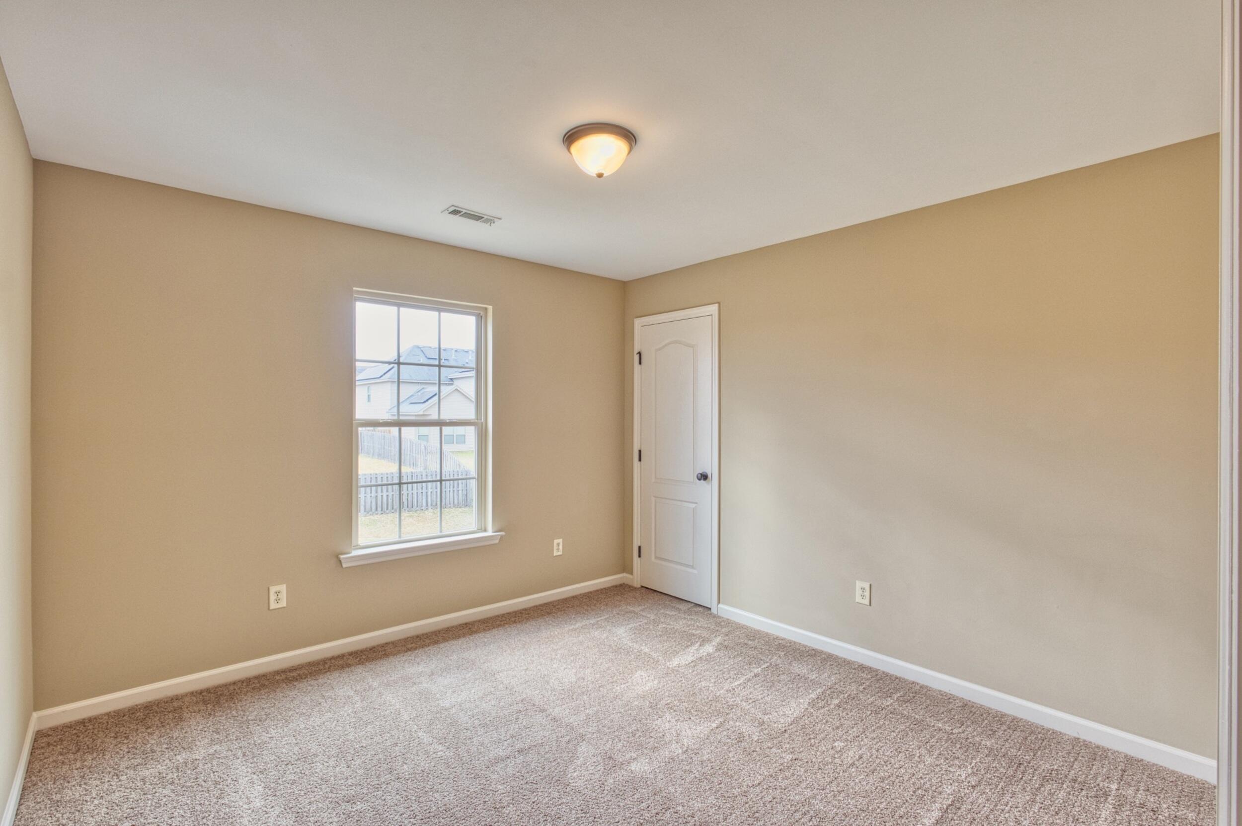 Empty bedroom with beige walls, carpet, a window, and a closed closet door.
