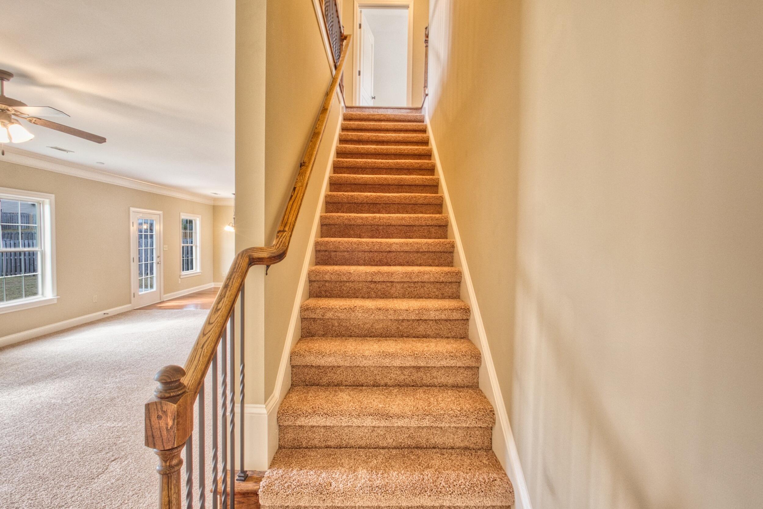 Carpeted staircase with a wooden handrail beside an empty living area.
