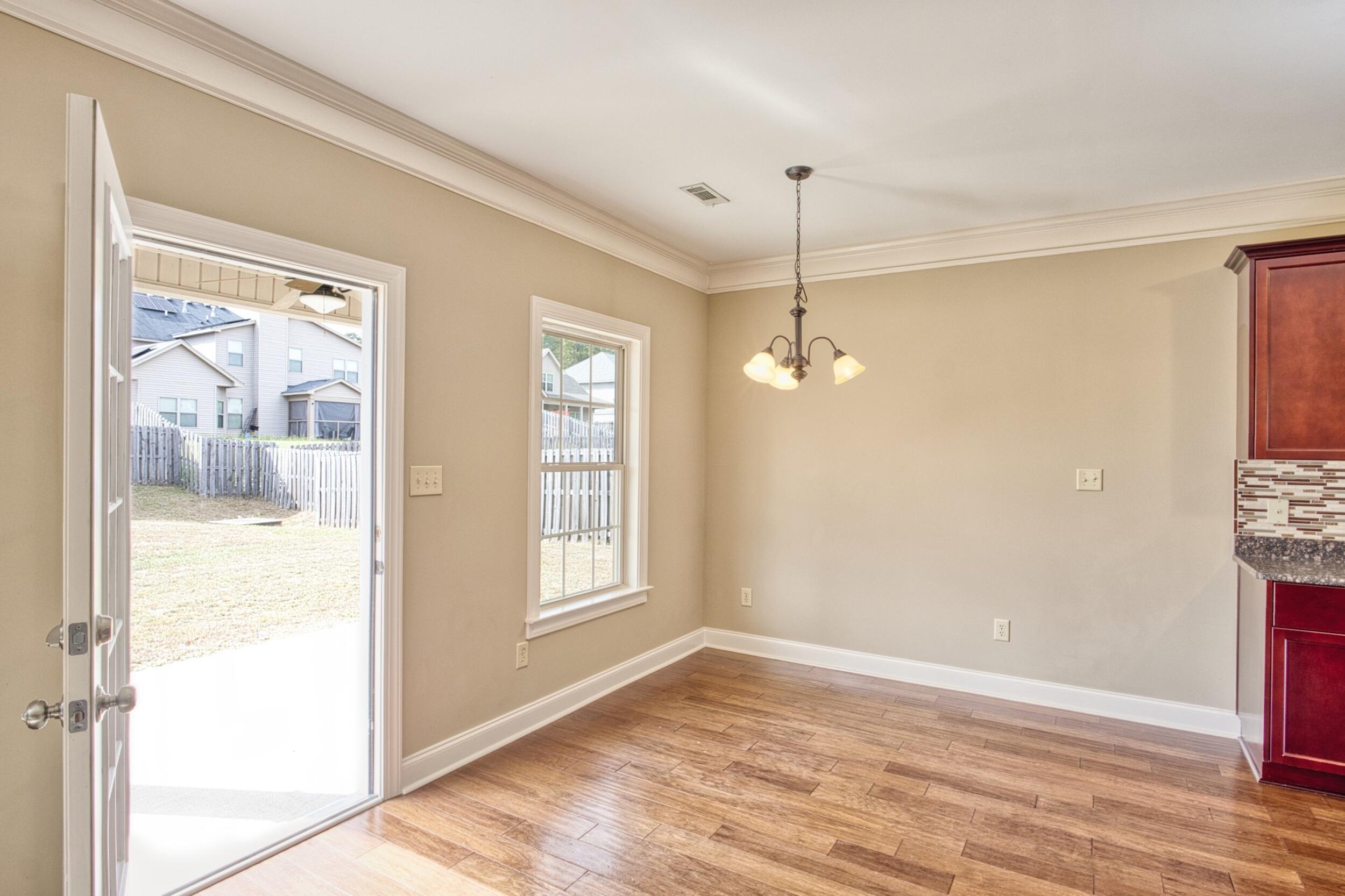 Unfurnished dining area with wood-look flooring, a hanging light, and an open door to the fenced backyard.