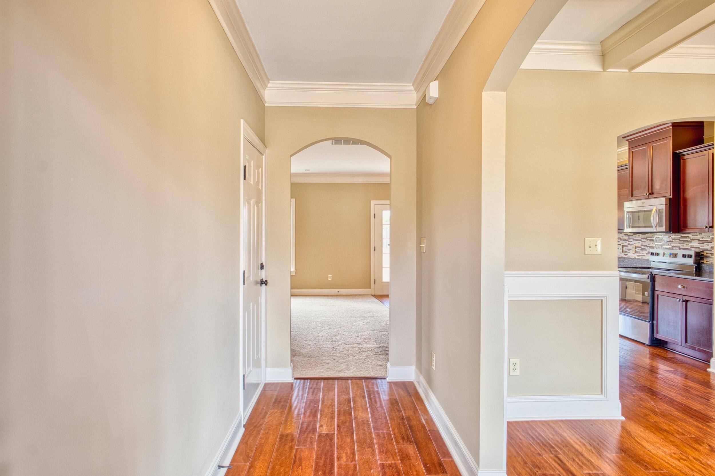 Hallway with reddish wood flooring and an arched doorway, with the kitchen visible to the right.