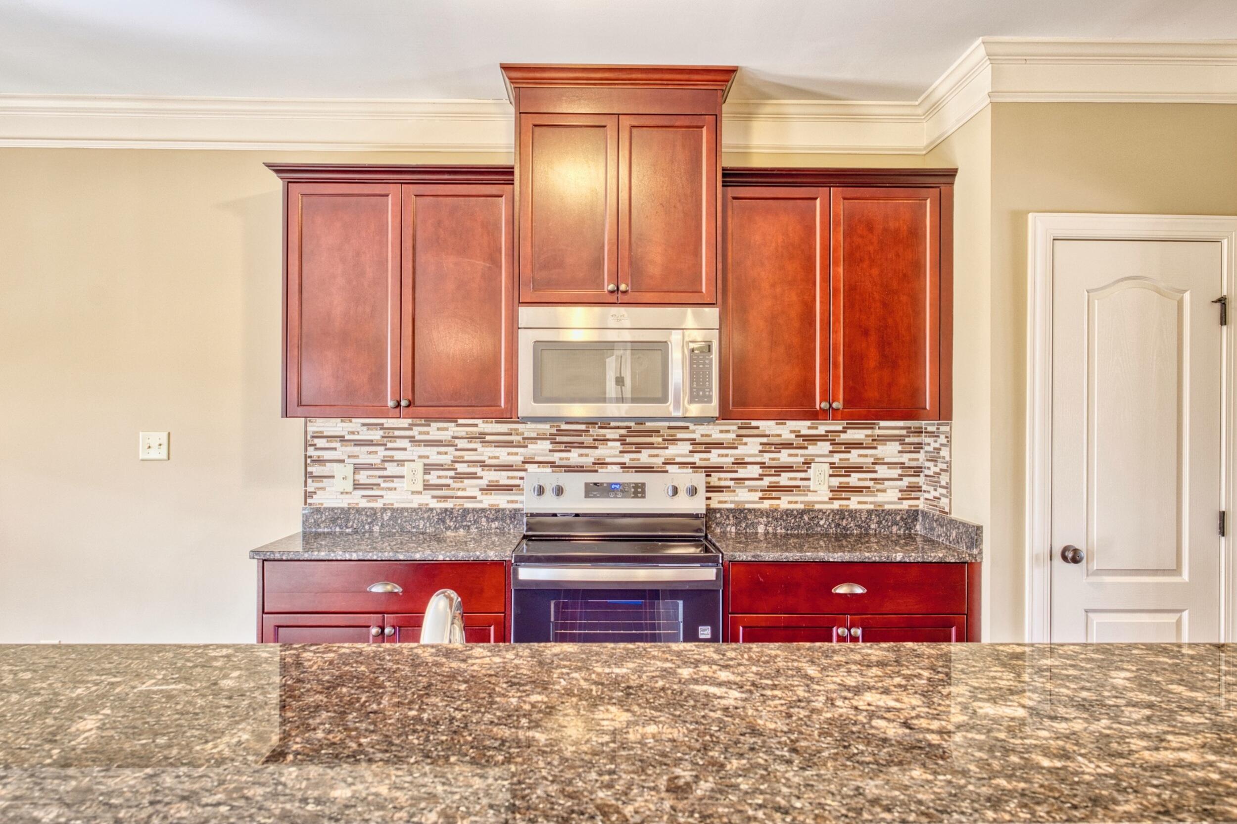 Kitchen with reddish-brown cabinets, stainless steel appliances, mosaic backsplash, and granite counters.