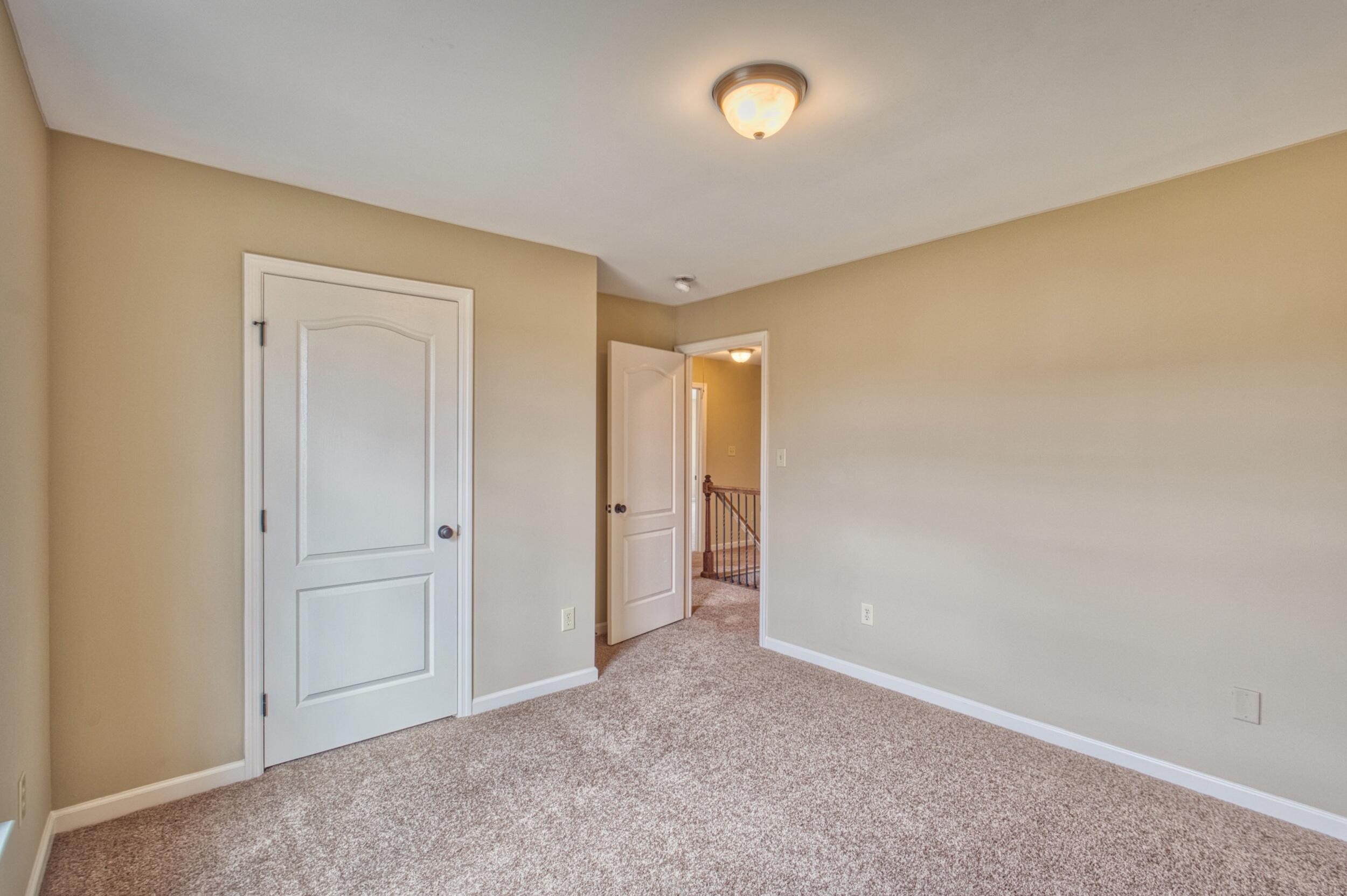 Empty bedroom with beige walls and carpet, opening onto a landing with a wooden railing.