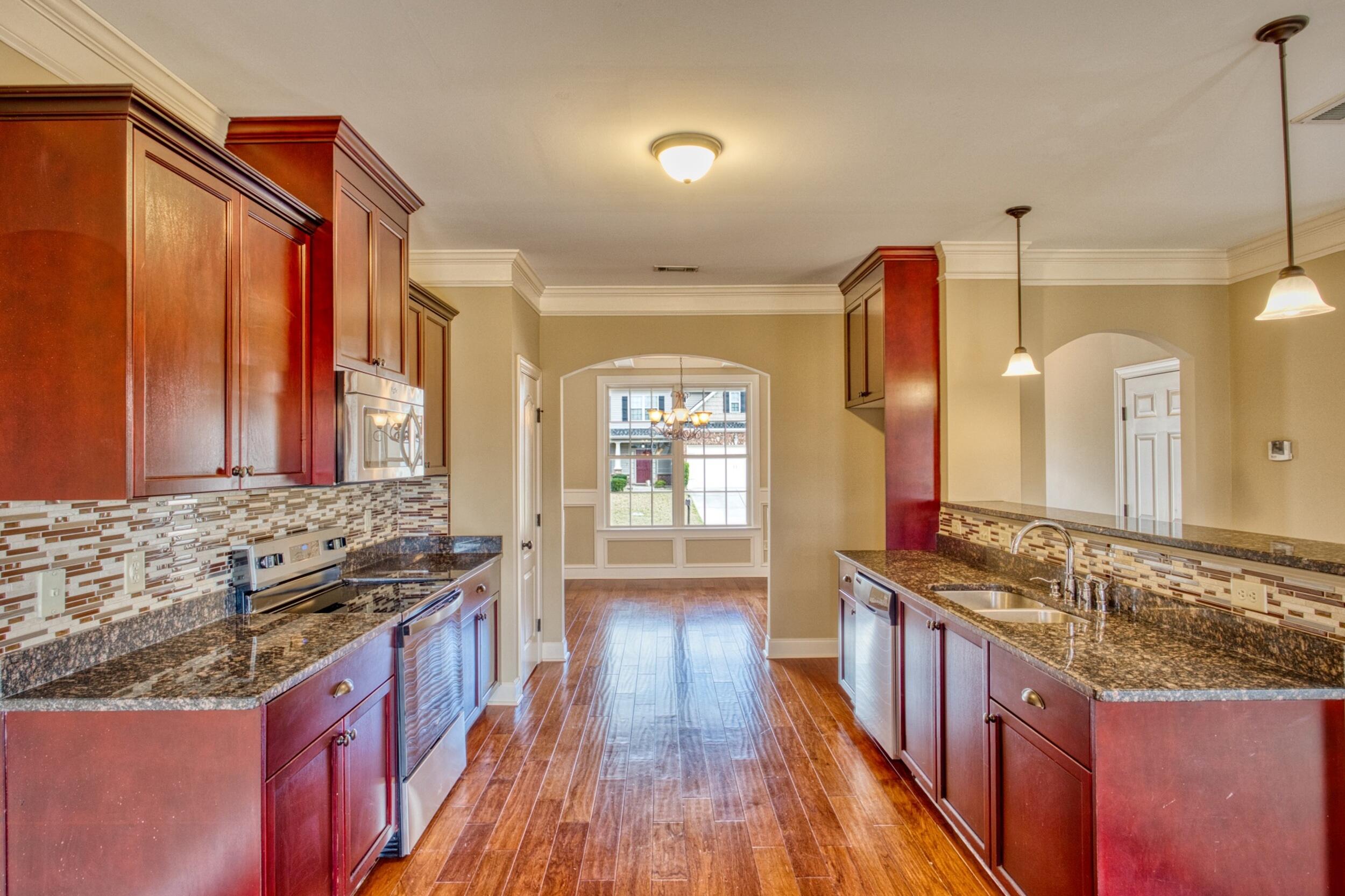 Kitchen with reddish wood cabinets, granite counters, and an arched opening to a bright dining area.