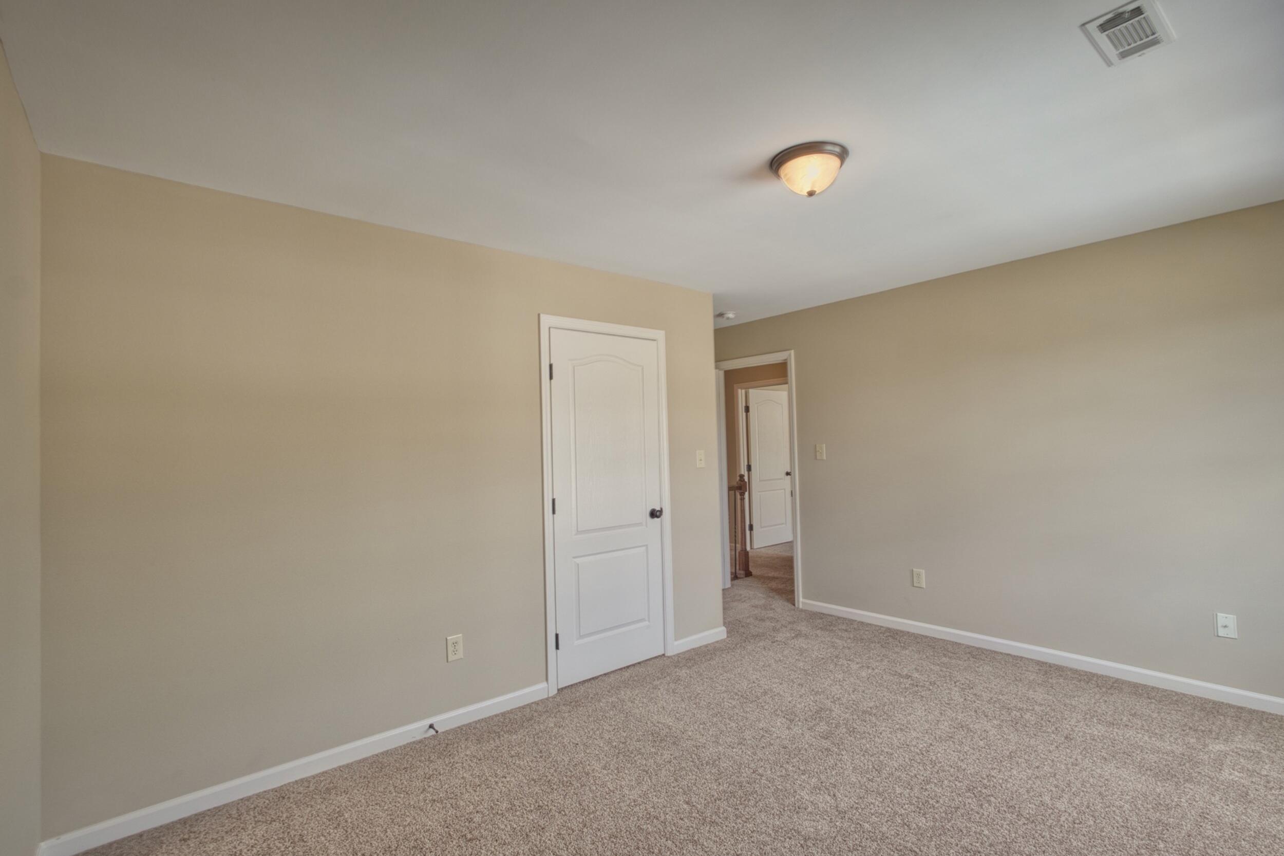 Empty carpeted room with beige walls, a white paneled door, and an open doorway to the hall.