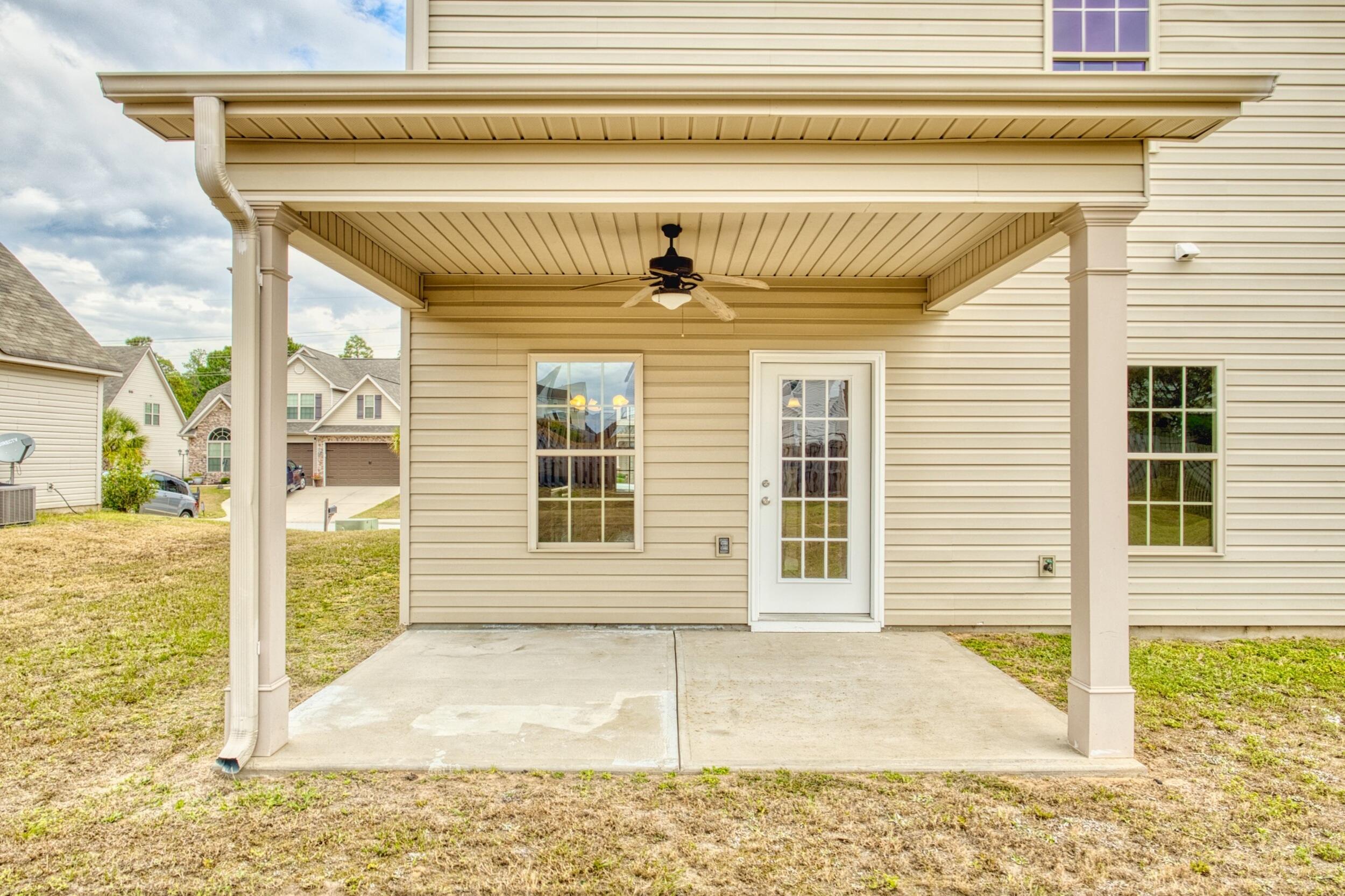 Covered concrete patio with white columns, ceiling fan, and glass-paneled back door.