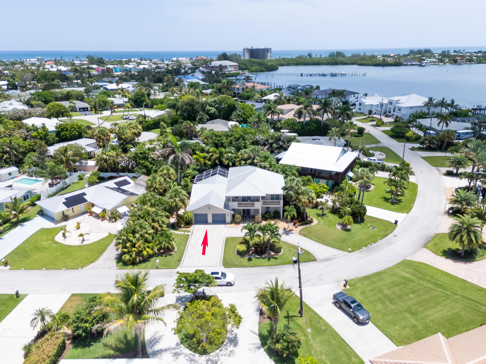 Aerial view of a white-roofed home marked by a red arrow, near a waterway and the ocean.