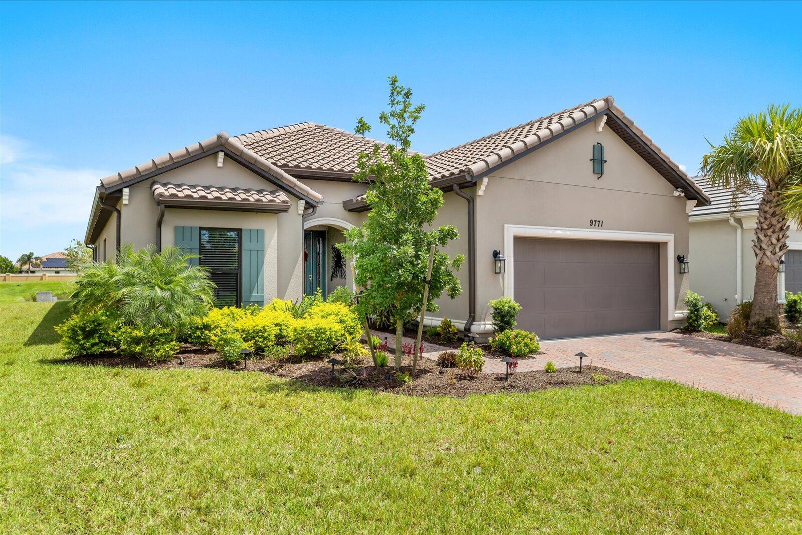 Single-story home with a tiled roof, teal shutters, and landscaped front garden beside a brick-paver driveway.