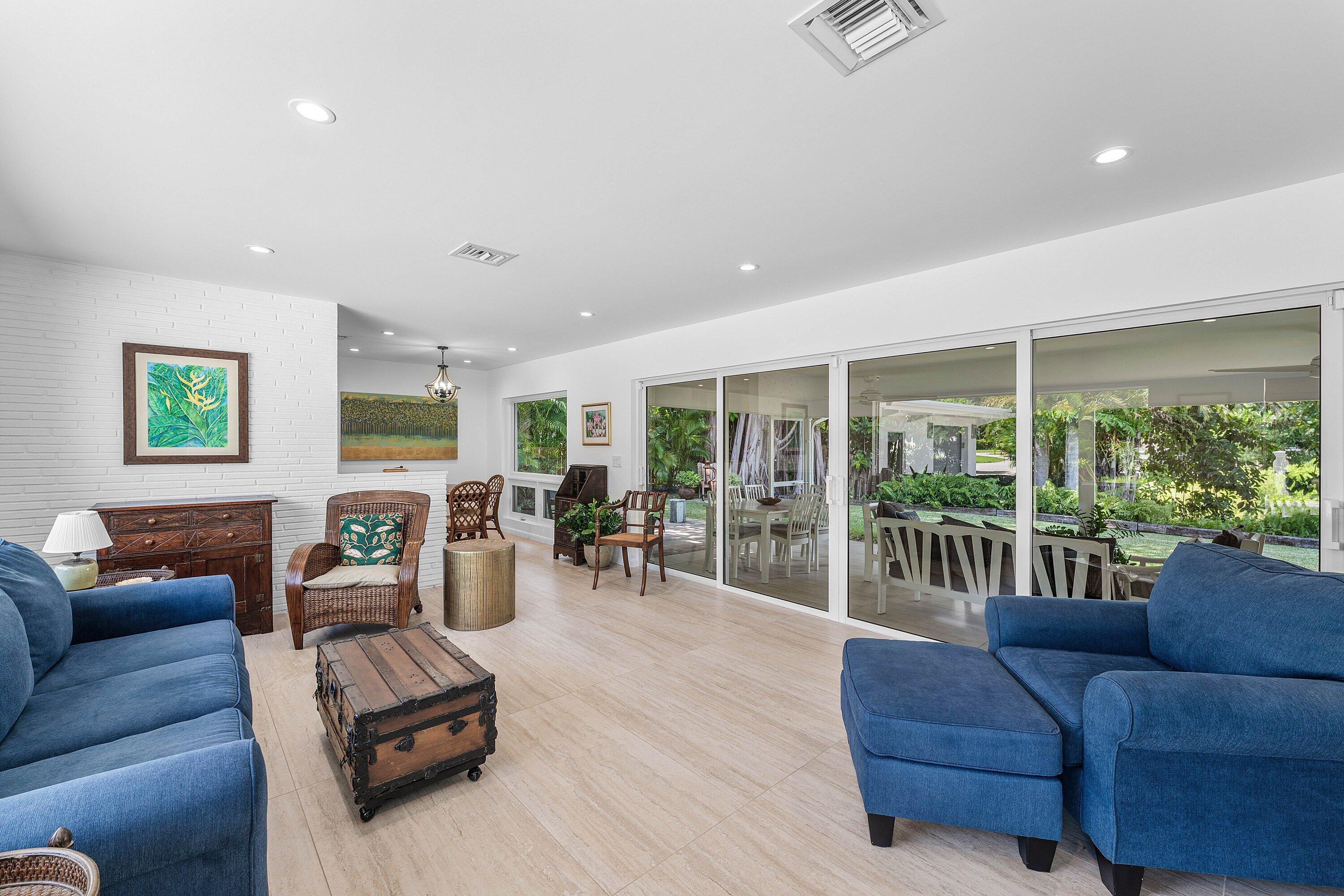 Living room with blue sofas and wicker chairs beside wide glass doors overlooking a leafy garden.