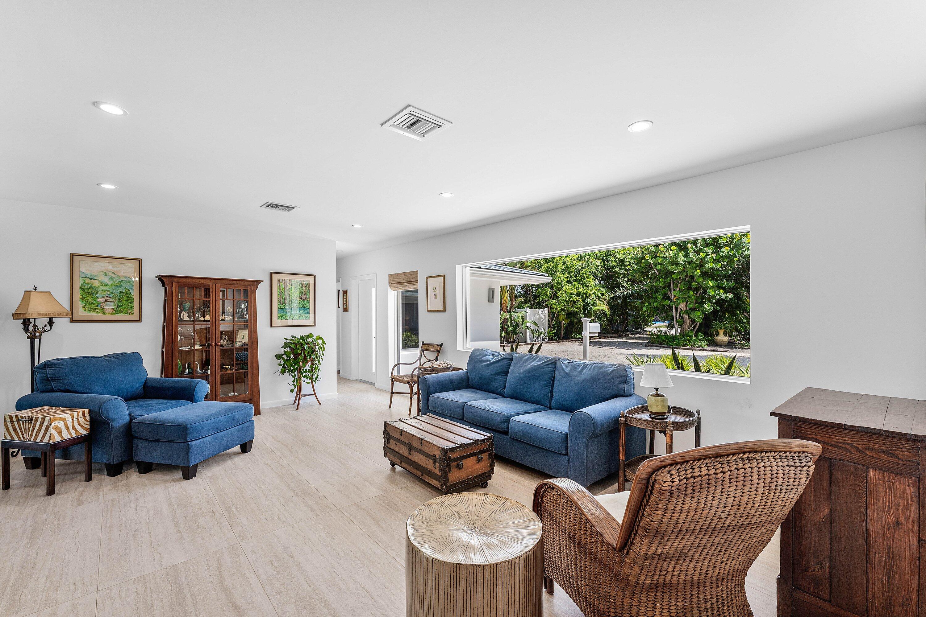 Furnished living room with blue sofas and a large window overlooking a leafy yard.
